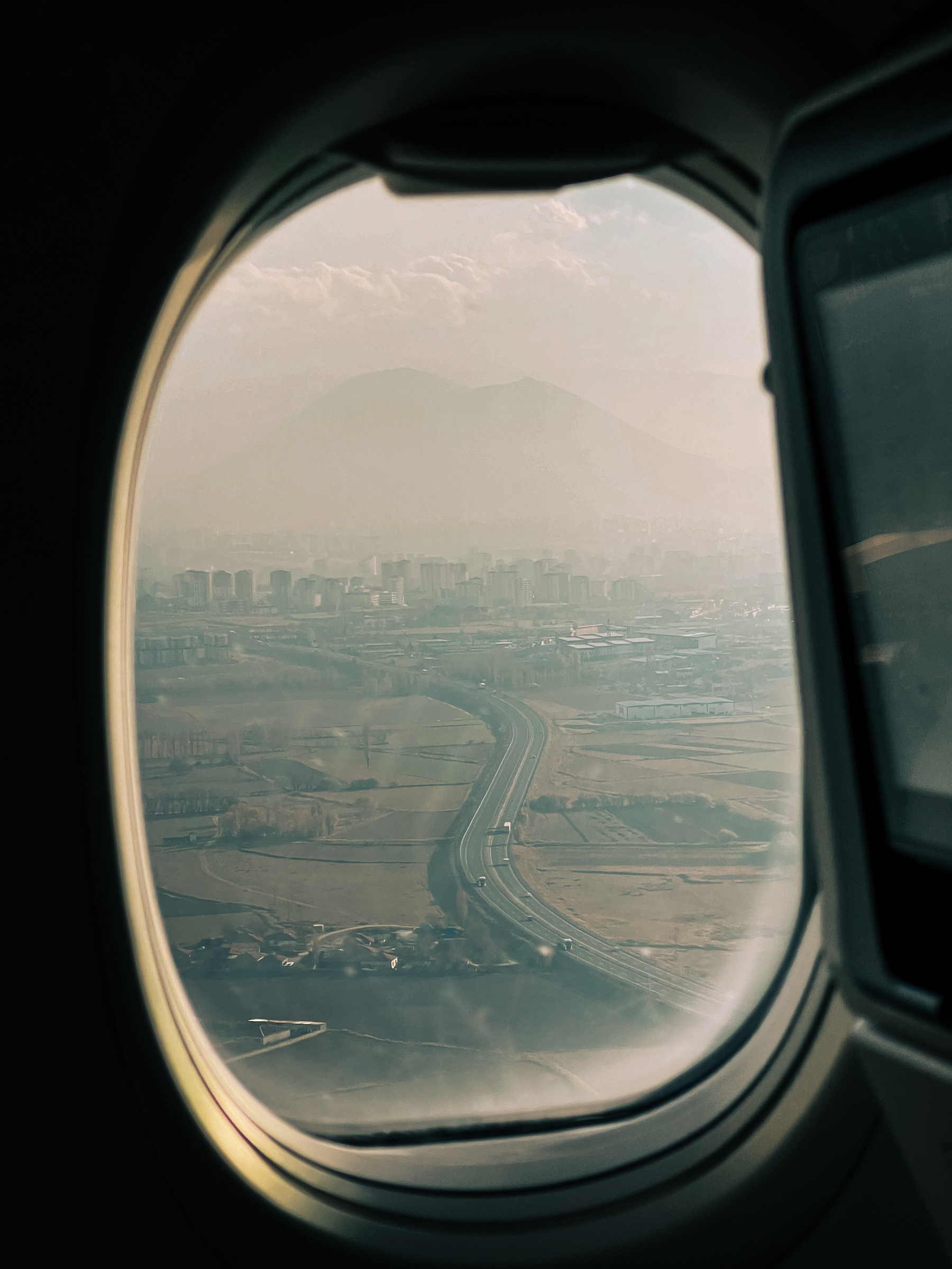Shot from inside an airplane, as it’s about to land. We can see a road, and a big mountain in the background. 