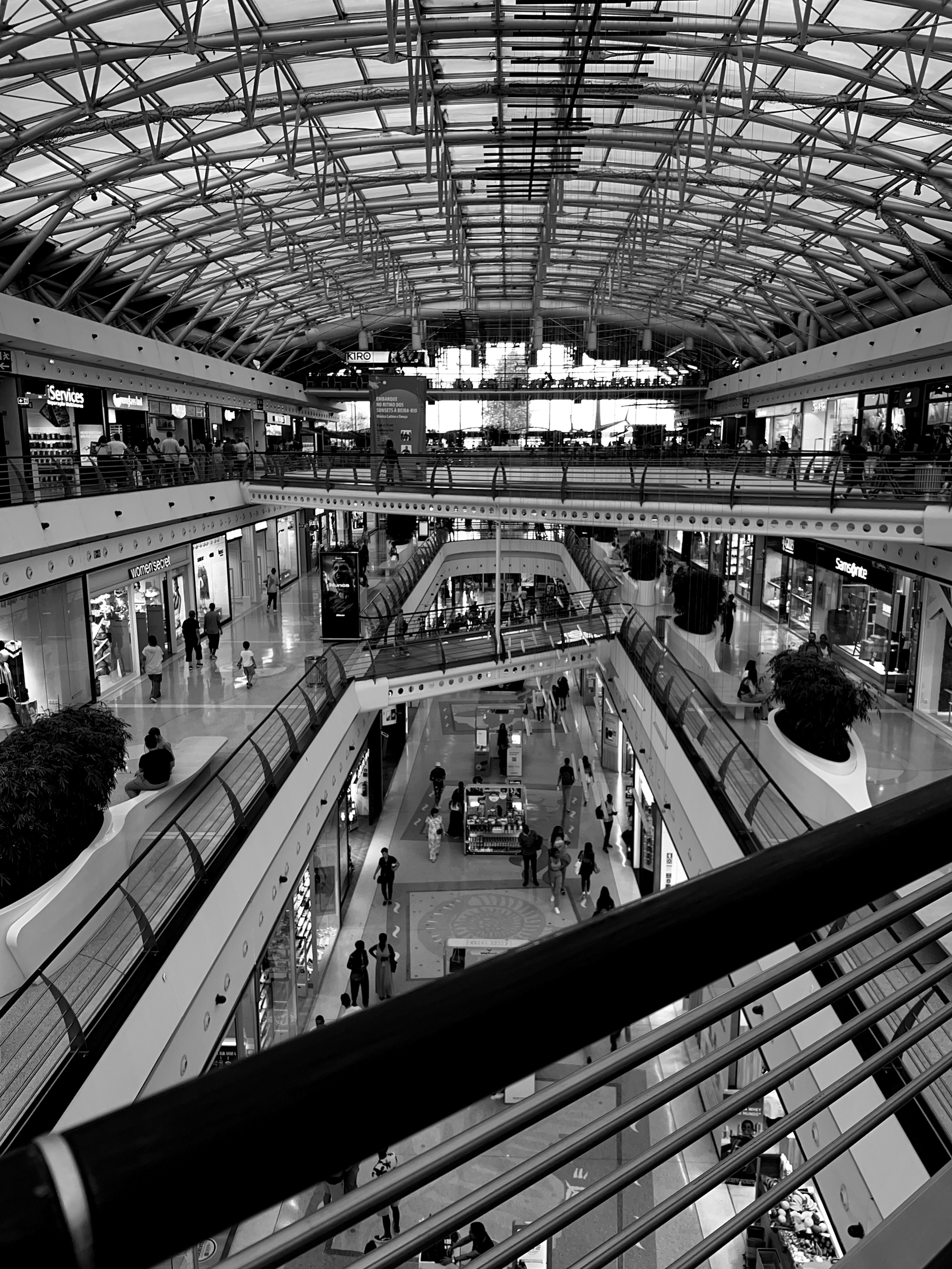 Black and white photo, inside of a mall. Looks a bit like the inside of a boat. 
