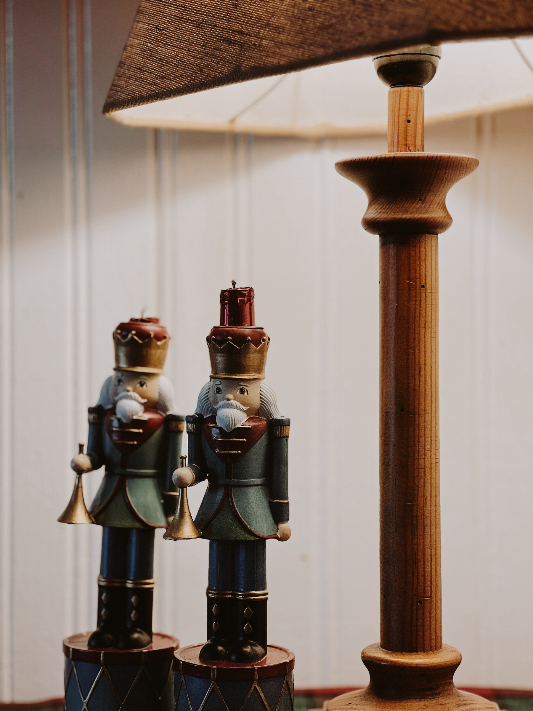 Two nutcracker figurines positioned on either side of a wooden lamp stand with a textured lampshade. The nutcrackers are ornately painted with blue uniforms, gold details, and red crowns.