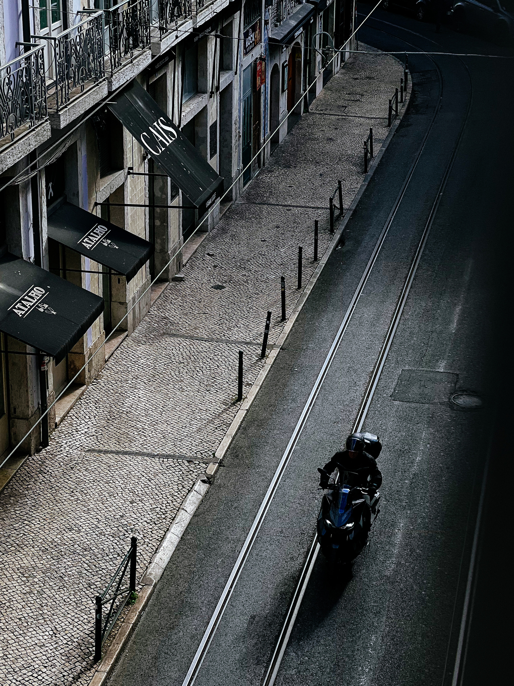 Looking down, a motorcycle rides on a street with tram tracks. 