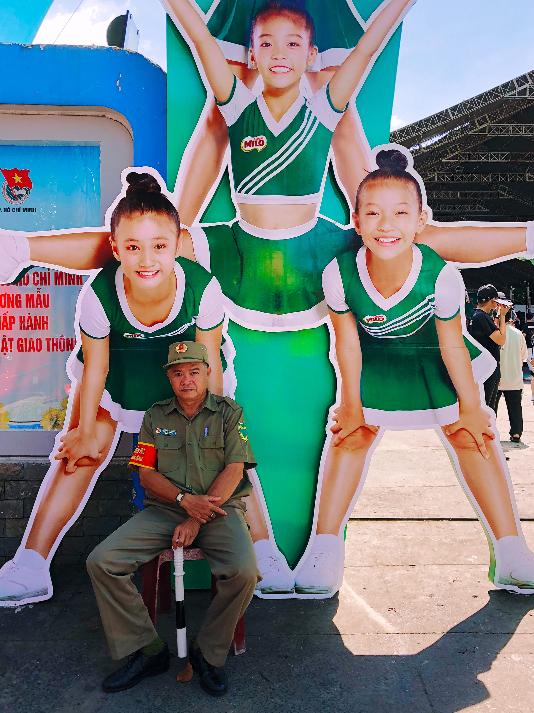 a security guard sits down in front of a cardboard cutout of three girls doing a gymnastics routine
