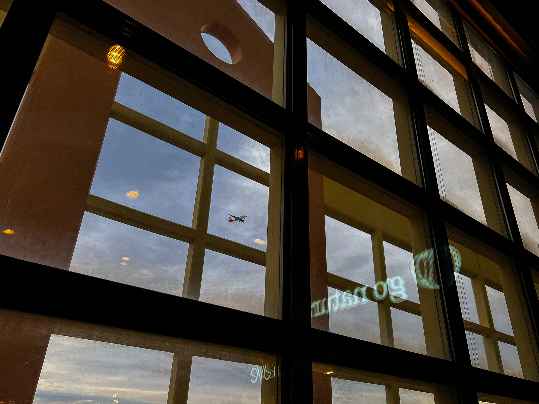 An airplane seen through large paneled windows, with warm indoor lighting and reflections on the glass.