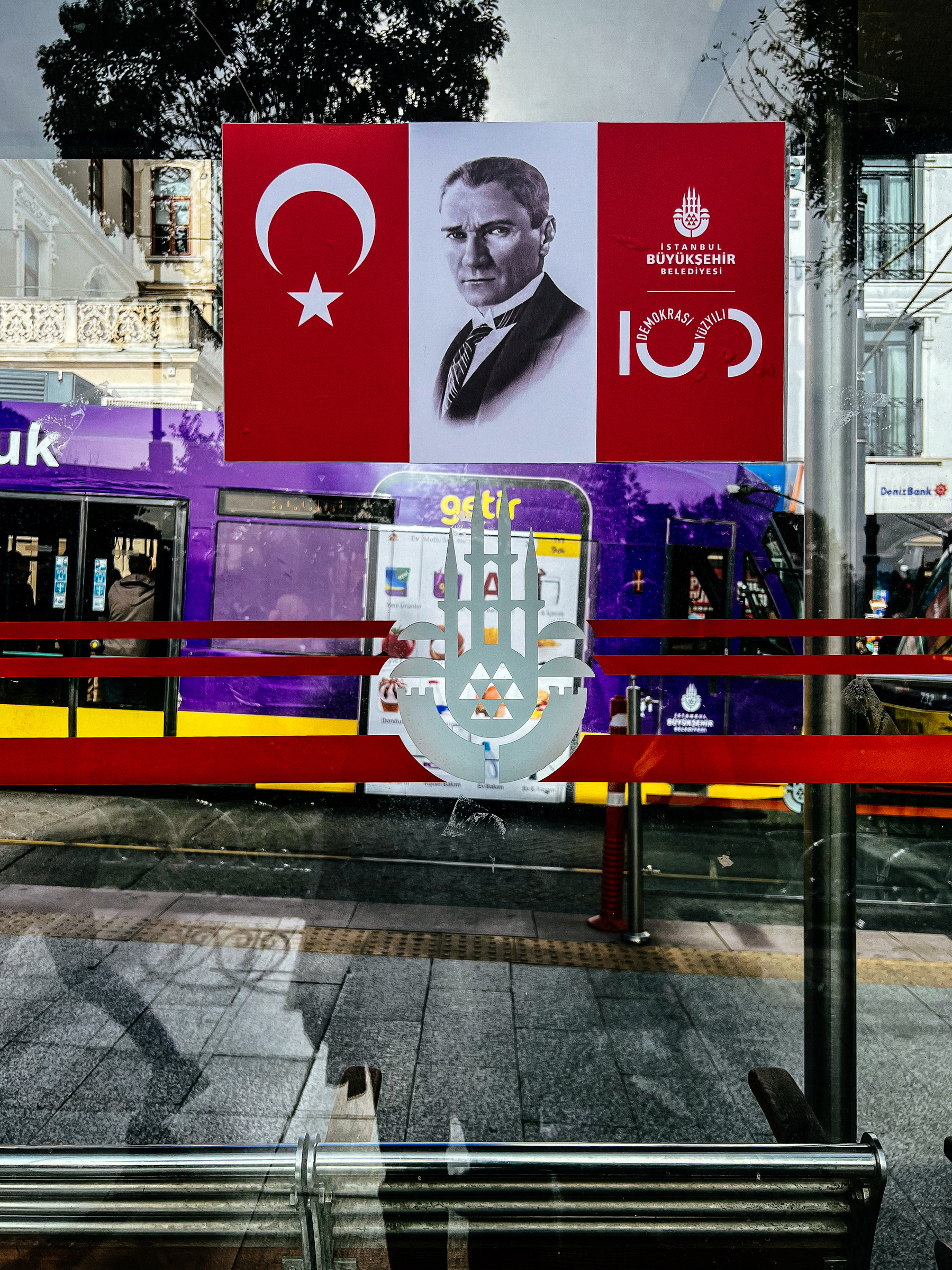 The Turkish flag, a portrait of Atatürk, and the logo of the 100th anniversary of the founding of Turkey. In a tram station.  