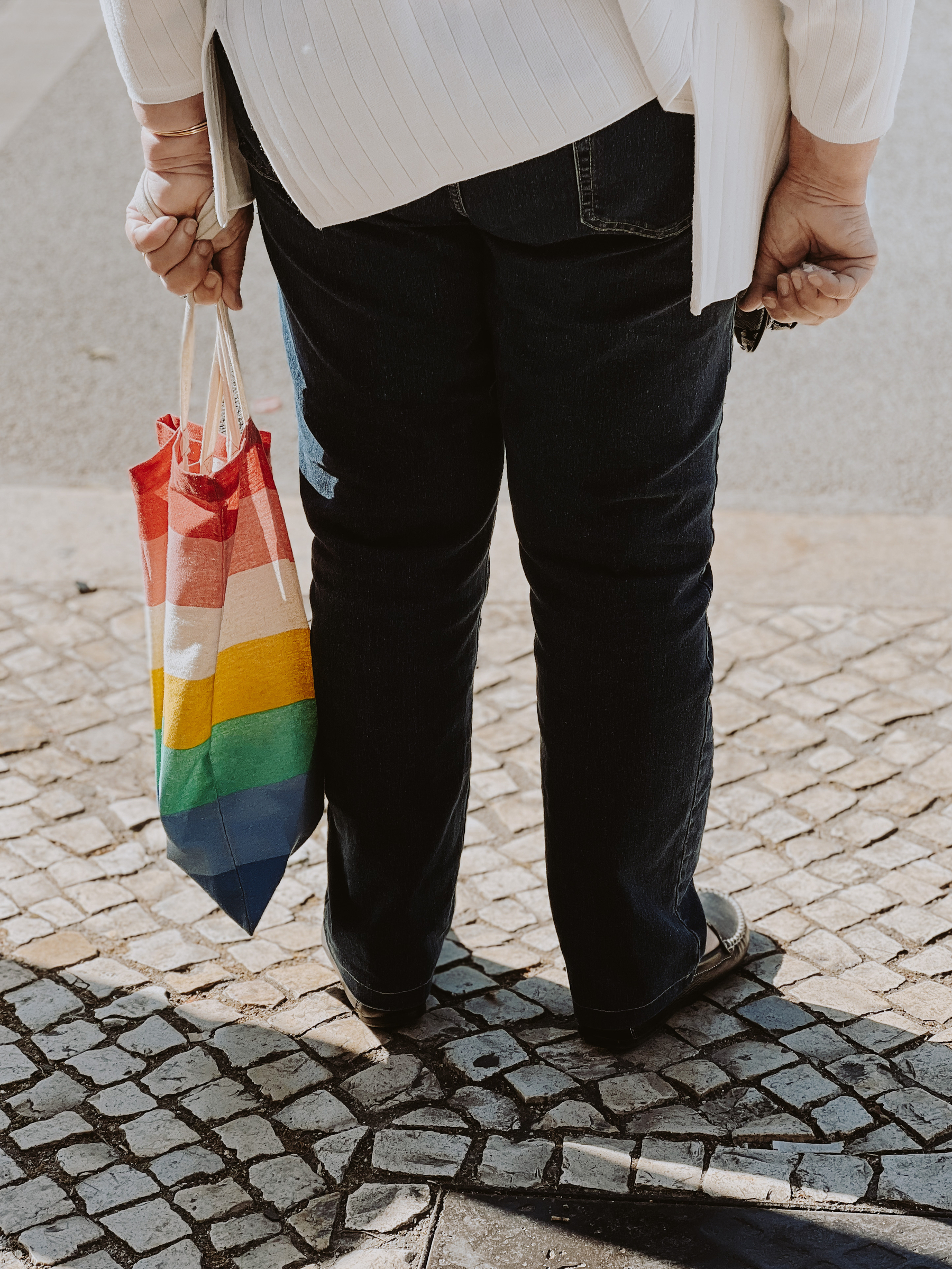 A woman holds a rainbow colored bag. 