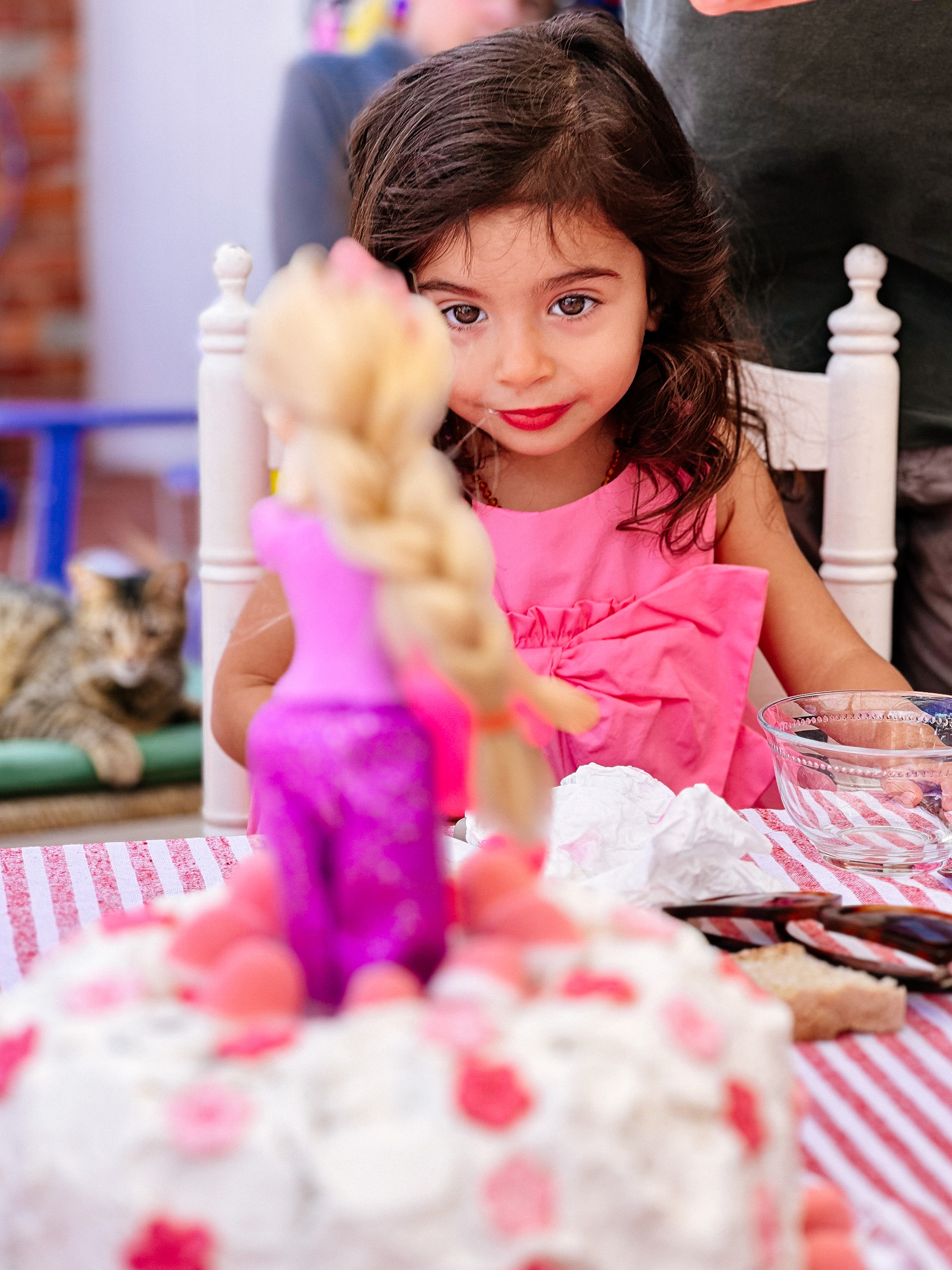 A girl looks at a doll on a cake. 