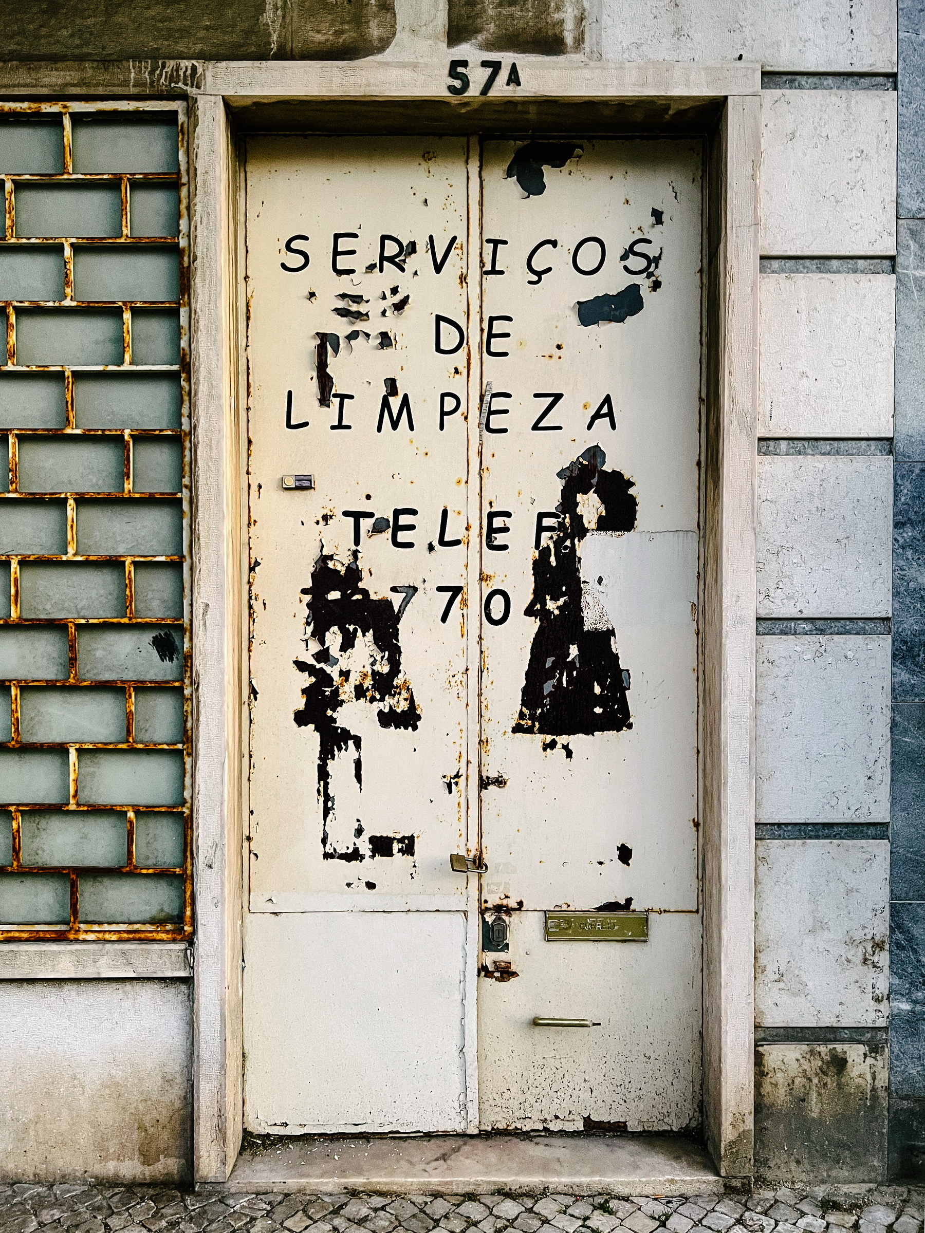 A door with the words “cleaning services” in Portuguese. The door is in an advanced state of disrepair. 