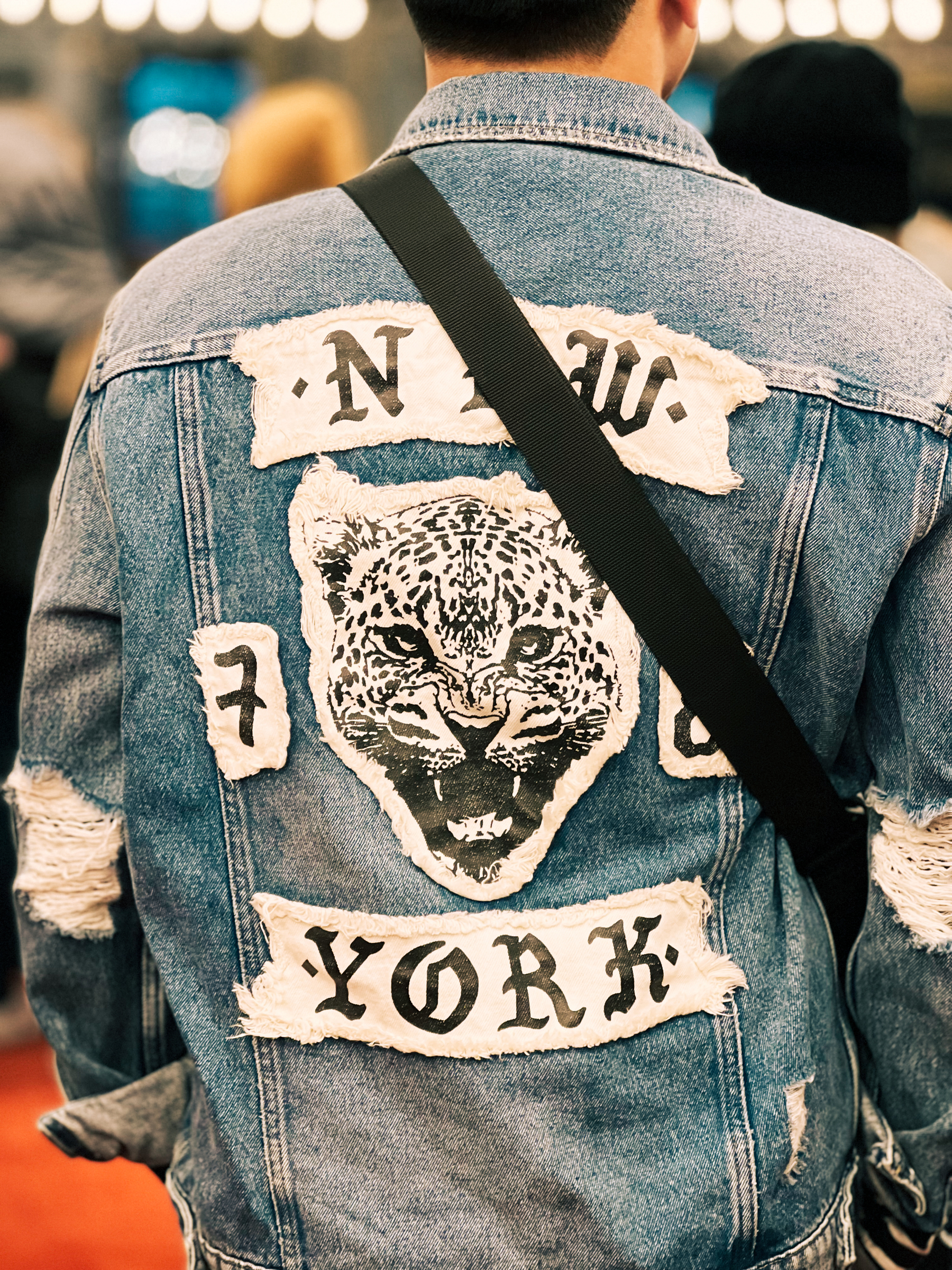 Person wearing a denim jacket with a large embroidered patch of a leopard&rsquo;s face and the words &ldquo;New York&rdquo; on the back.