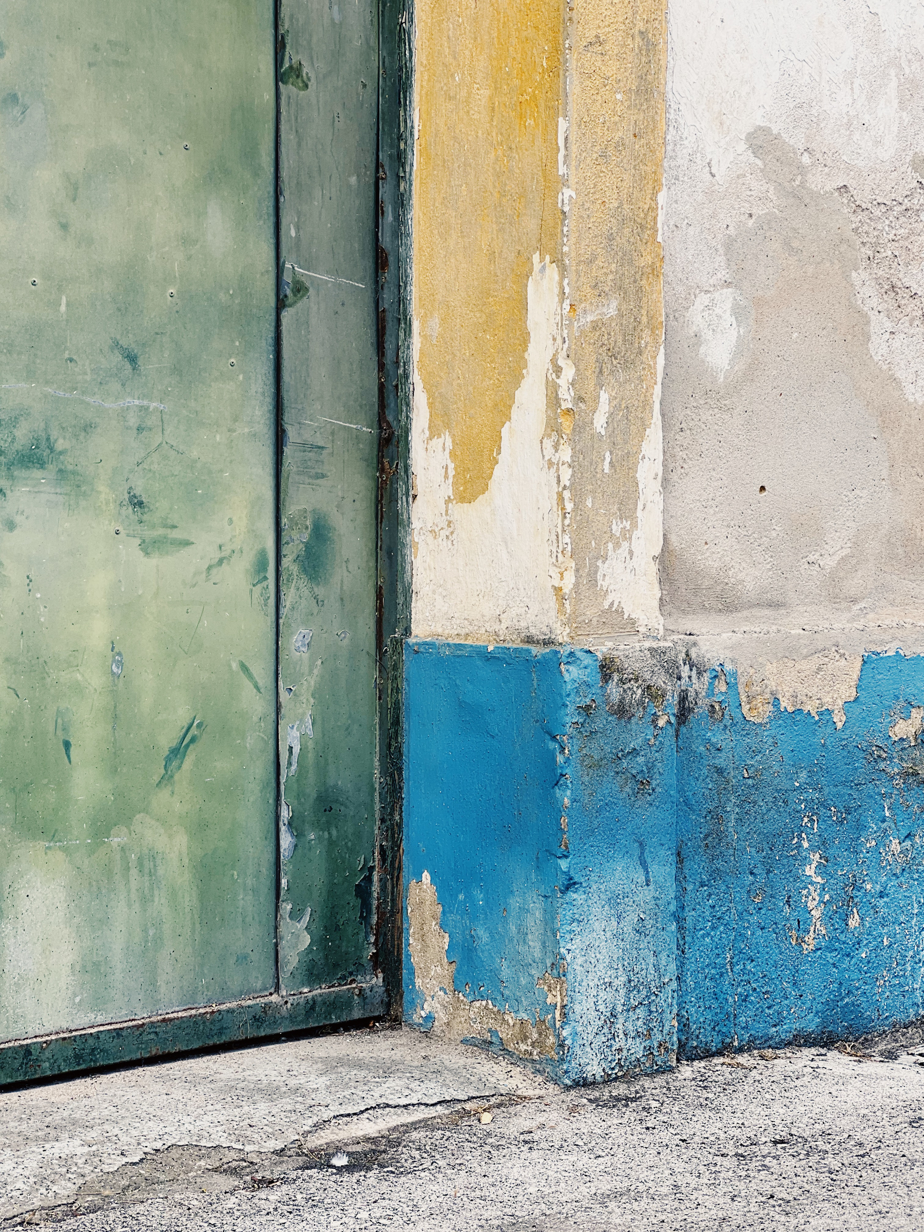 A faded green metal door, with a faded blue and yellow wall. 
