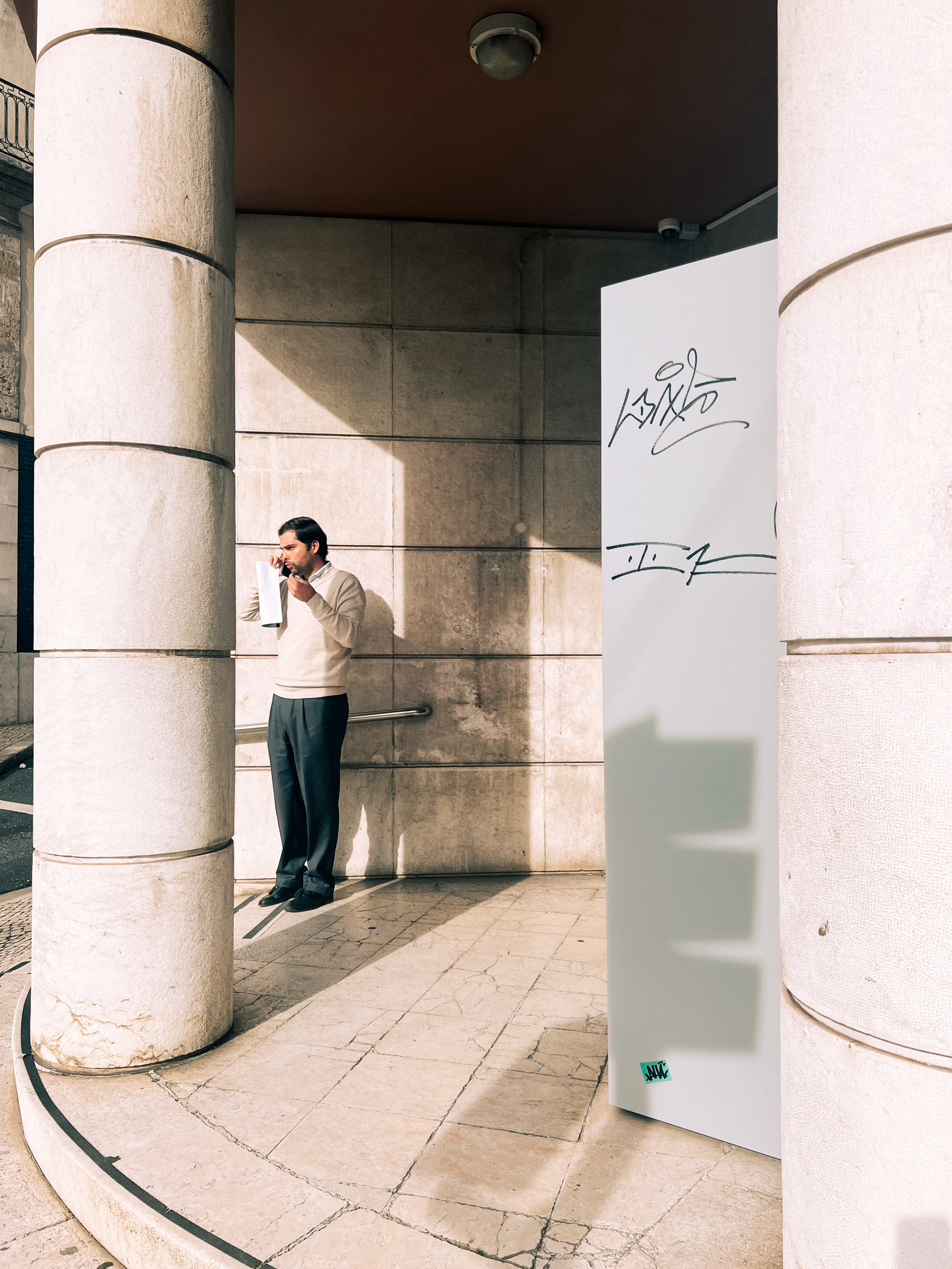 A man talks on the phone. He’s blending perfectly into the columns around him.