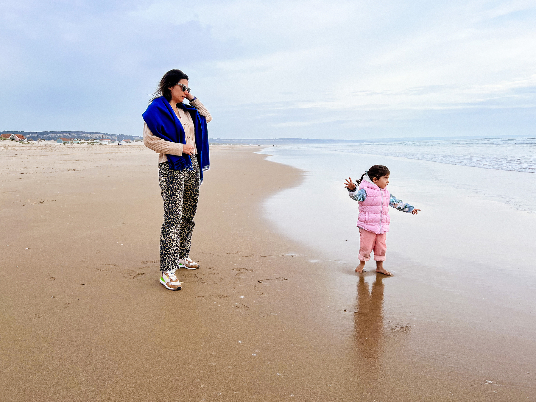 A mom and a toddler at the beach, looking out to the sea. 