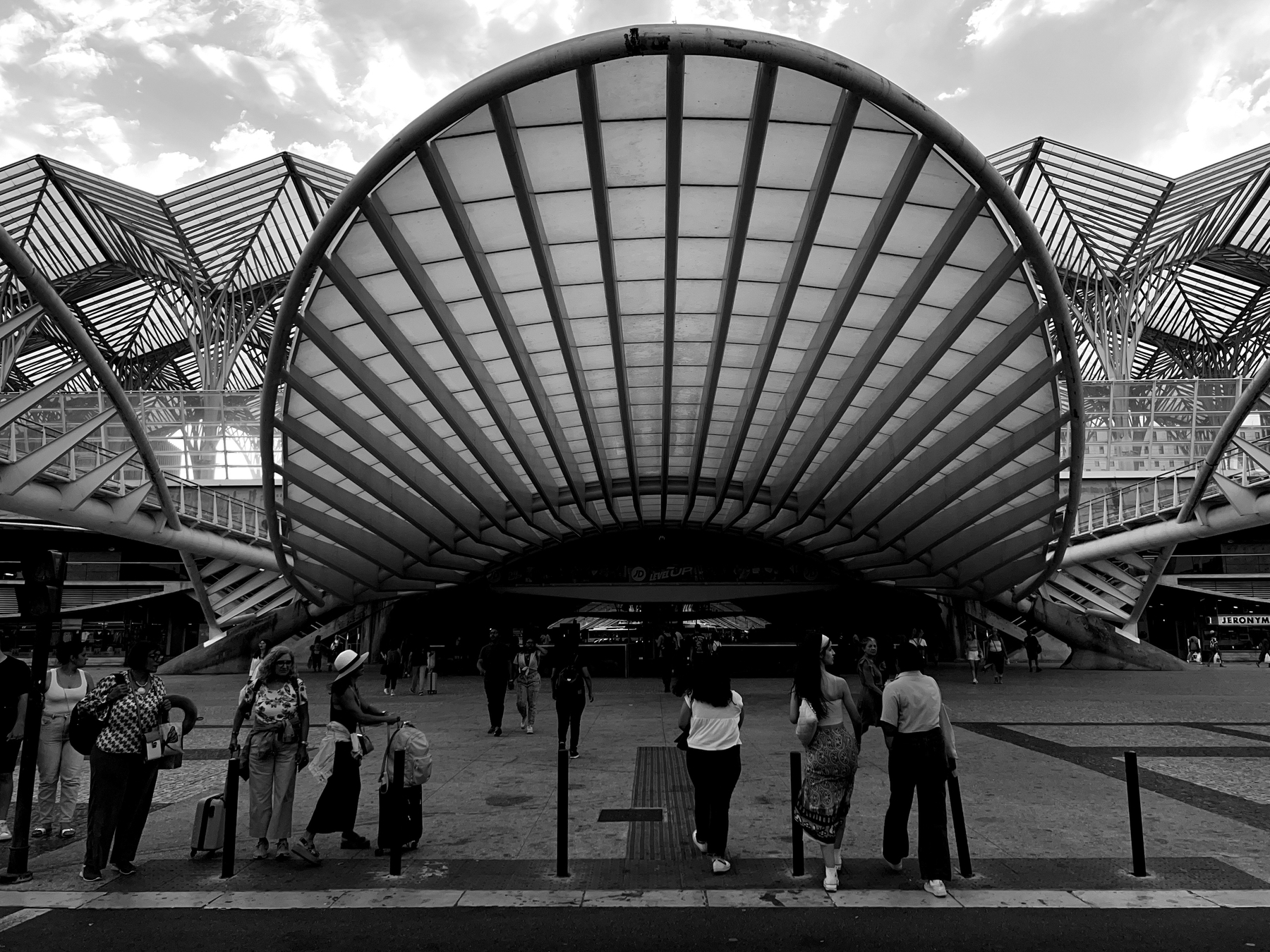 Black and white photo, people stand by a modern looking building. 