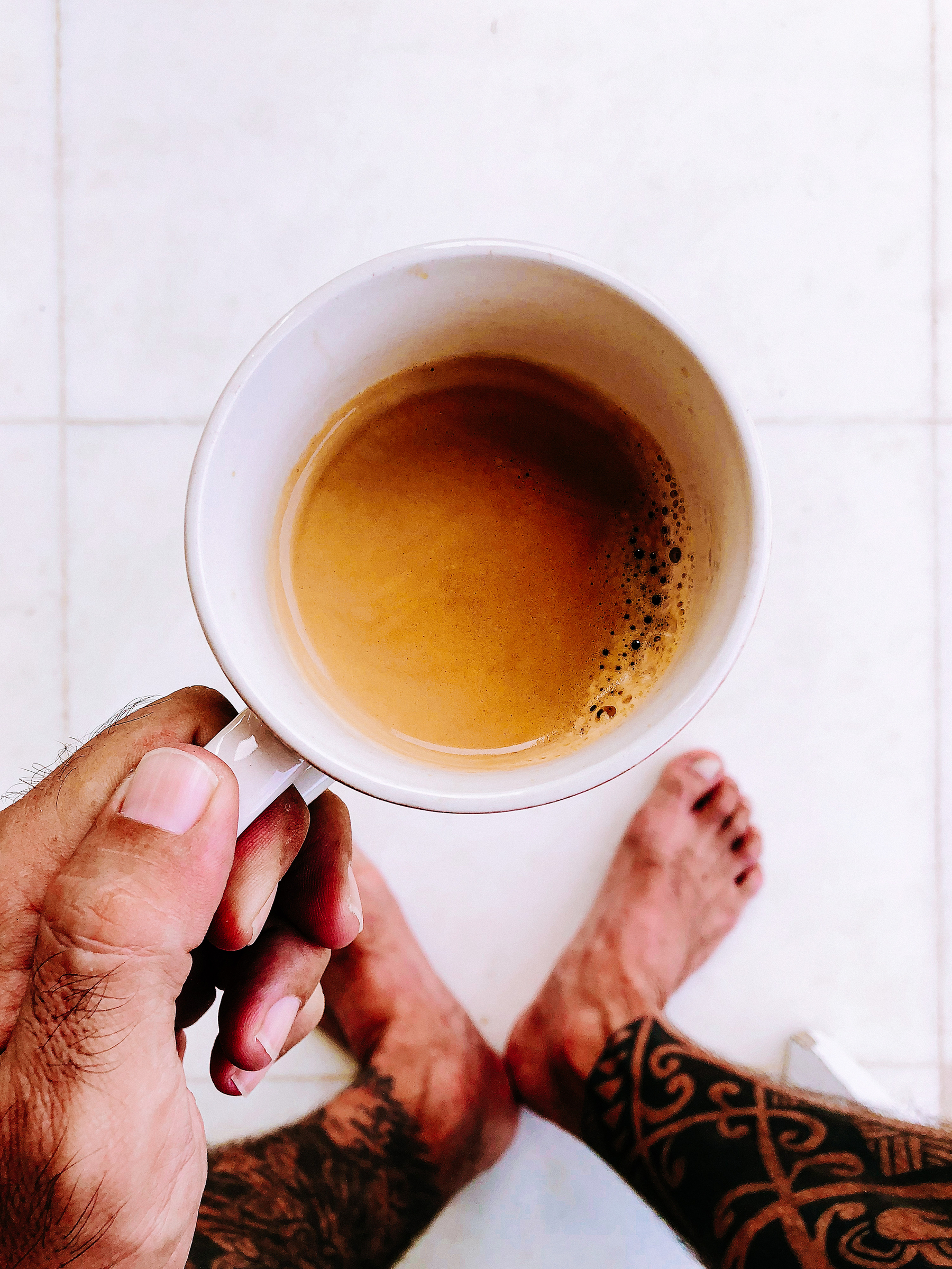 looking down on a hand holding a cup of coffee. We can also see tattooed legs.