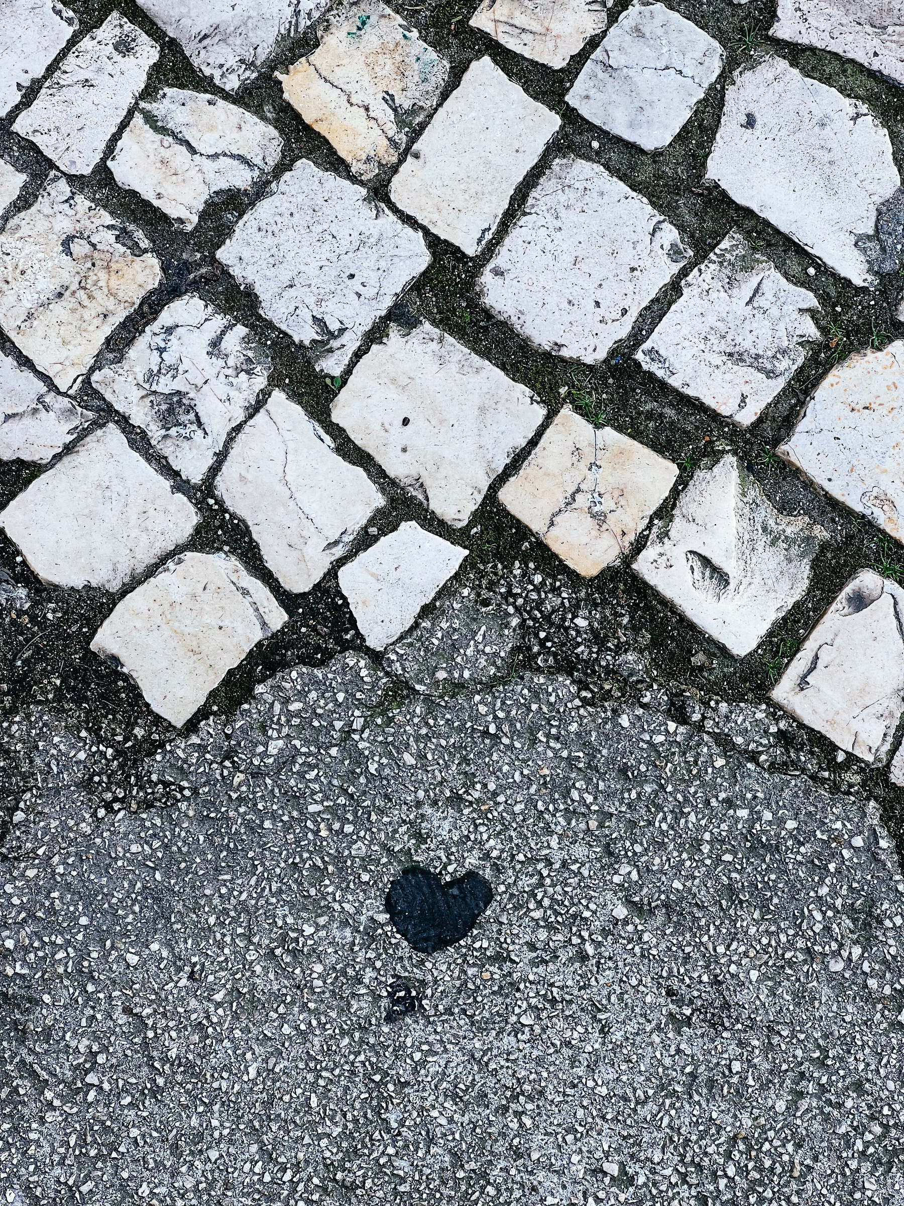 Looking down, pavement with a heart shaped piece of something. Gum?