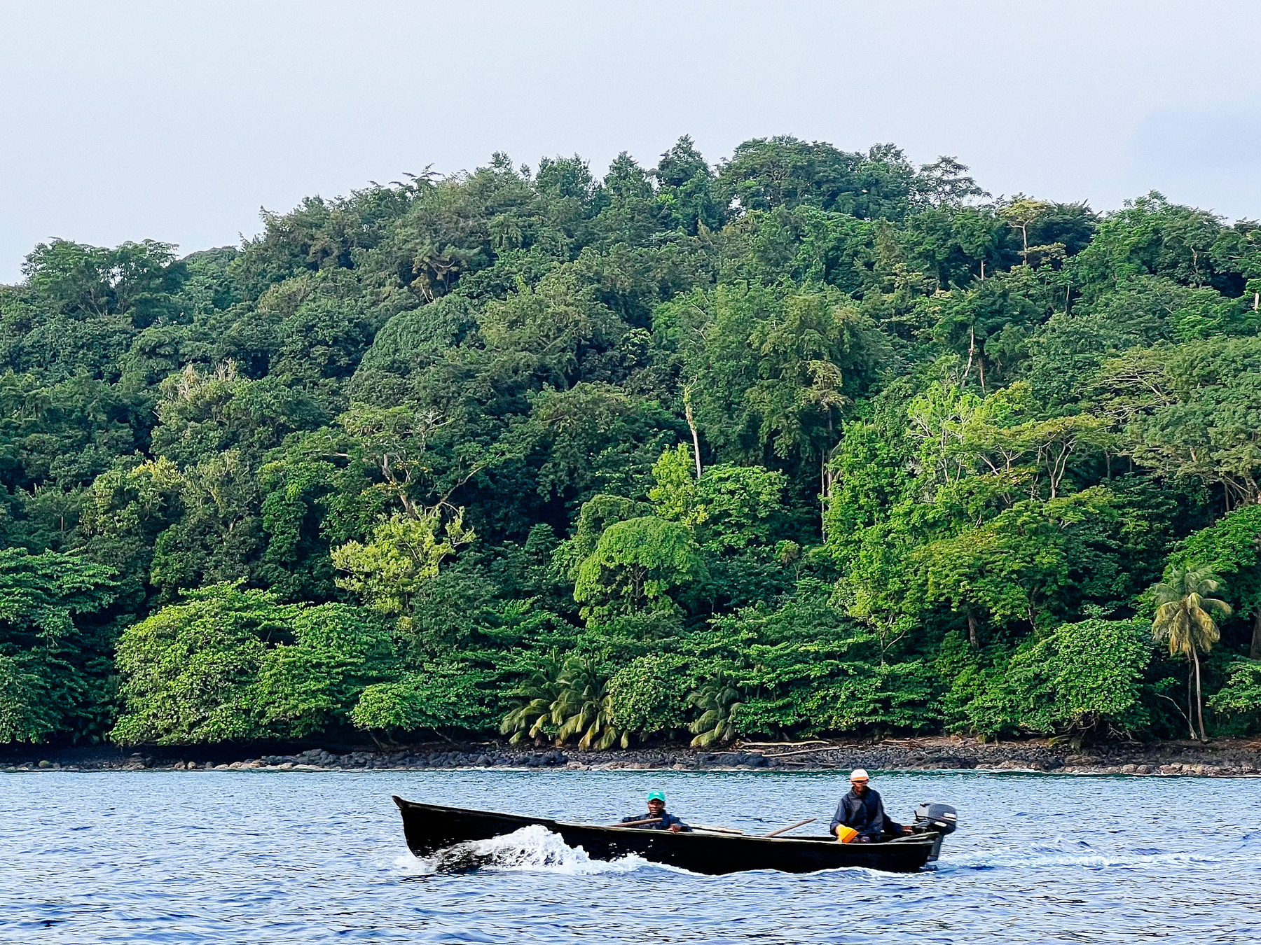 A couple of fishermen on a boat, with rainforest in the background. 