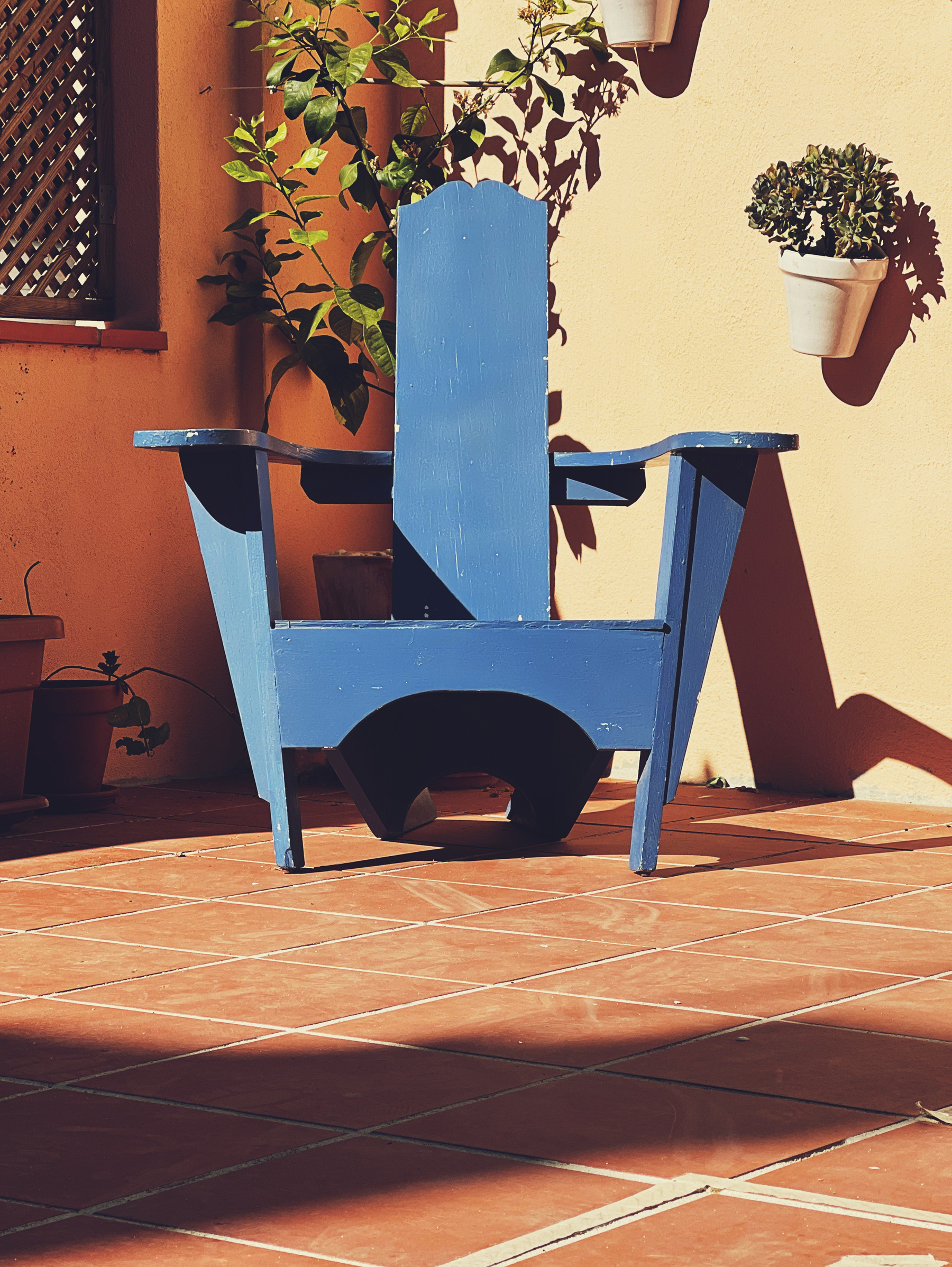 A chair in the corner of a patio, with some plants close by. 
