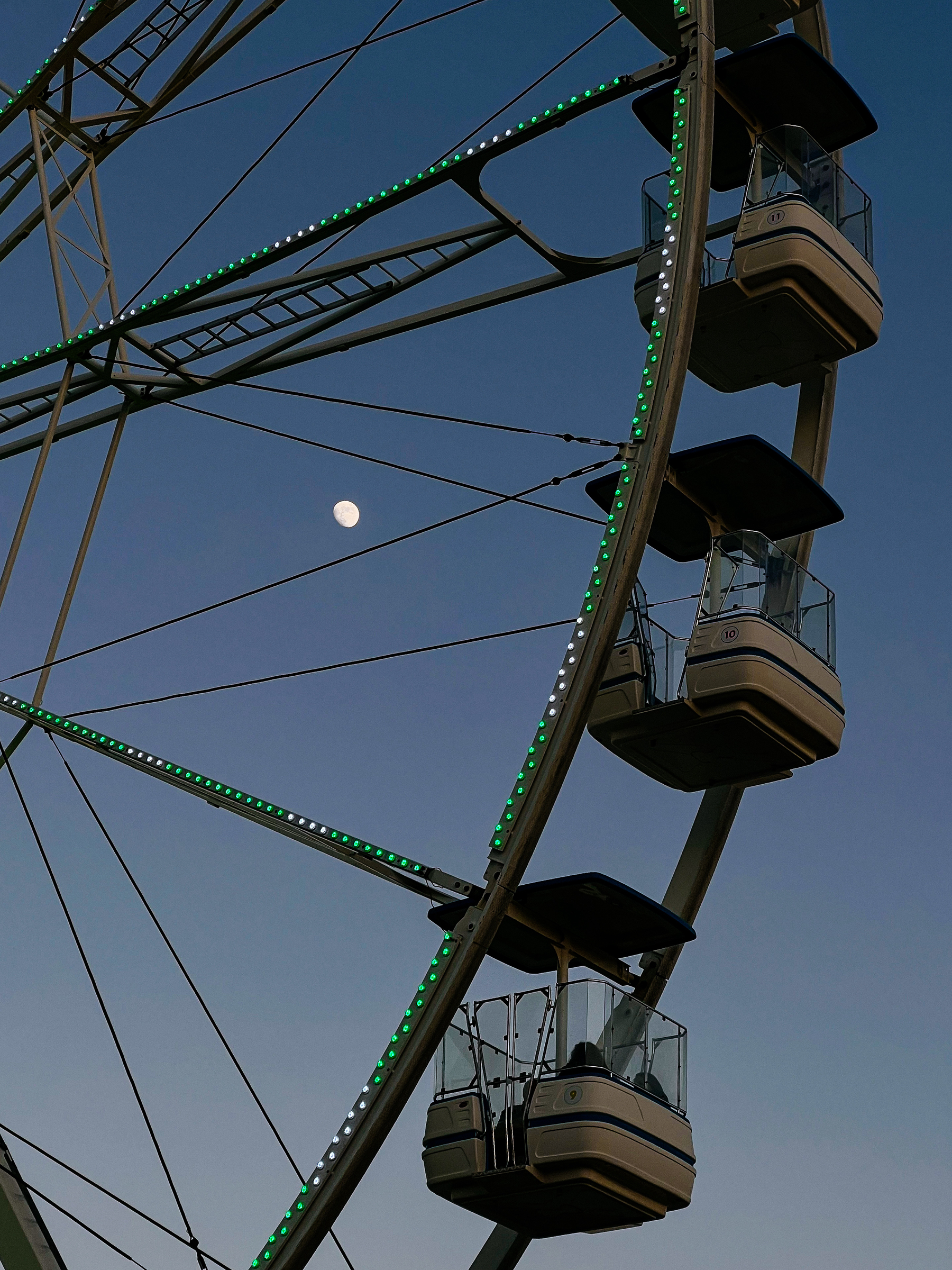 A Ferris wheel with illuminated green lights against a twilight sky, with the moon visible in the background.