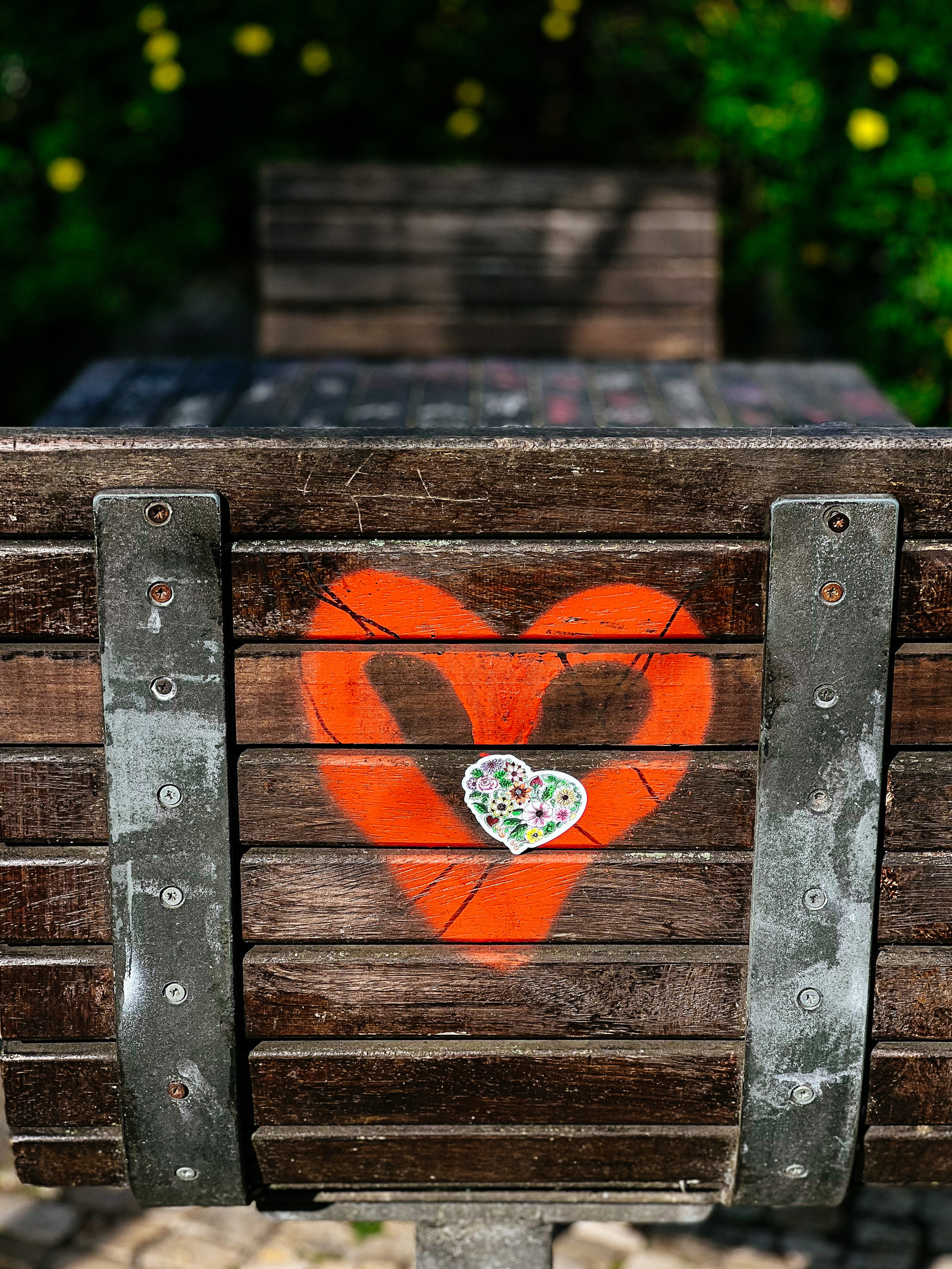 A heart sticker glued to the back of a chair. The chair also has a heart graffitied. 