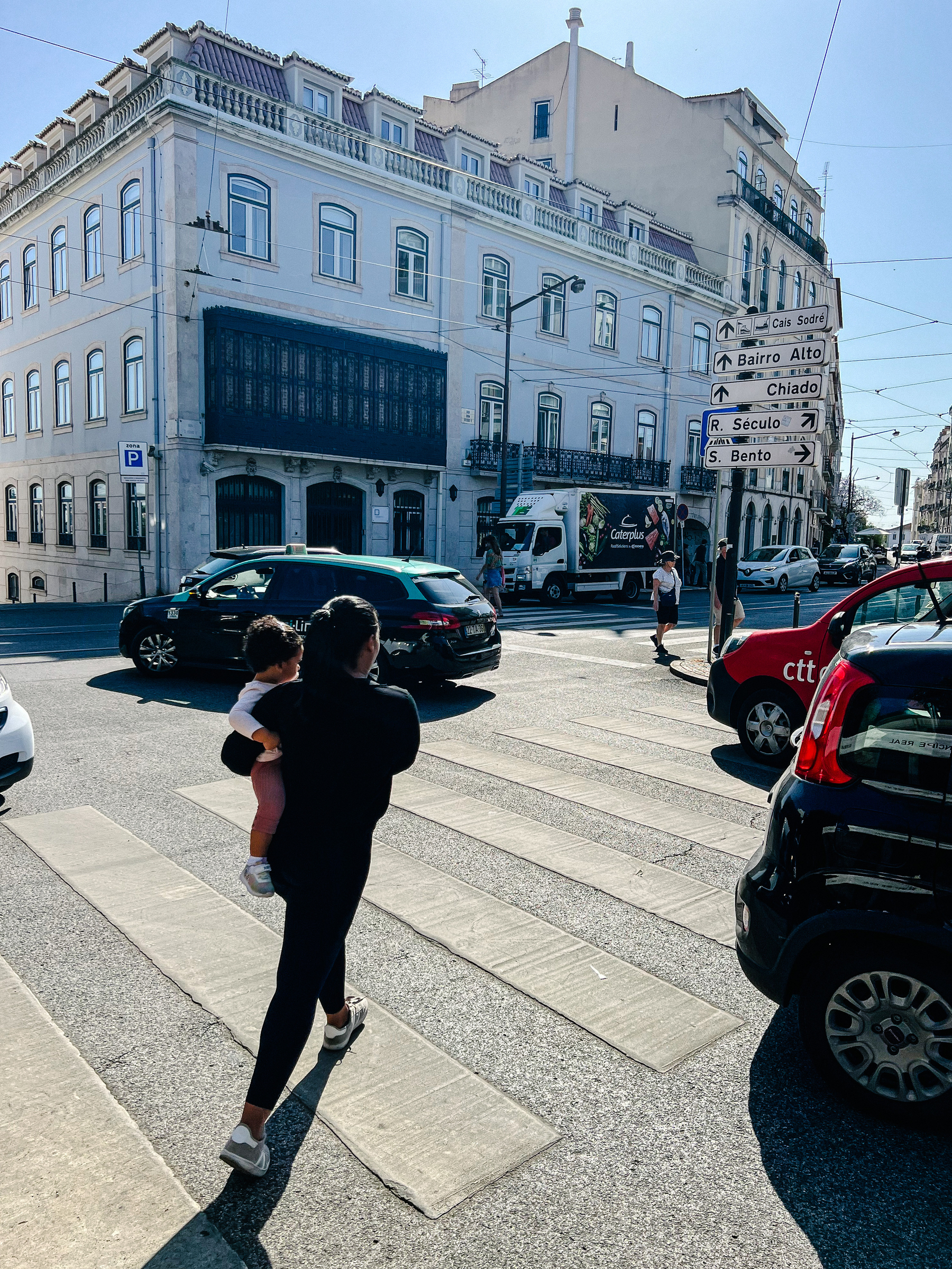 A mother walks across a sidewalk, cars all around her. 