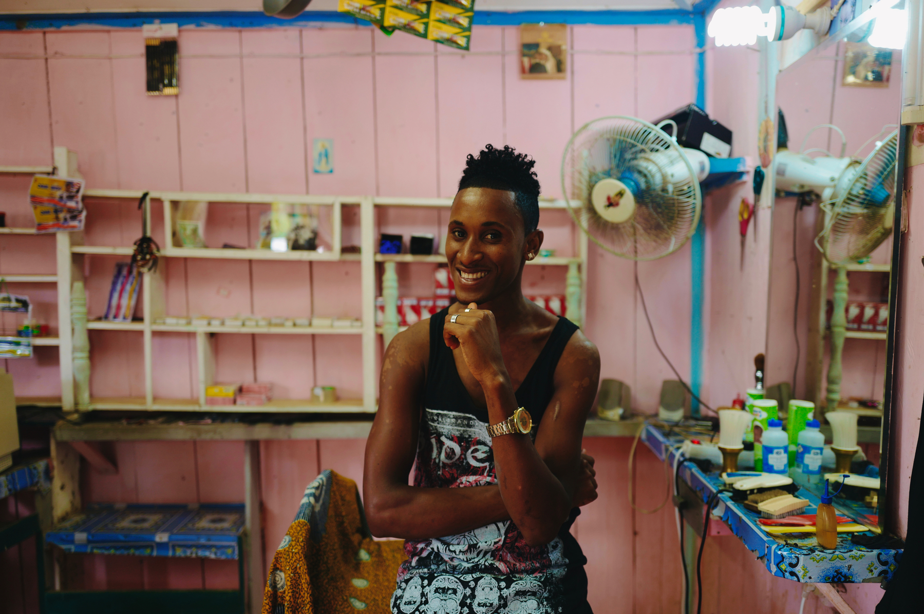 A man smiles at the camera, inside his pink colored barber shop. 