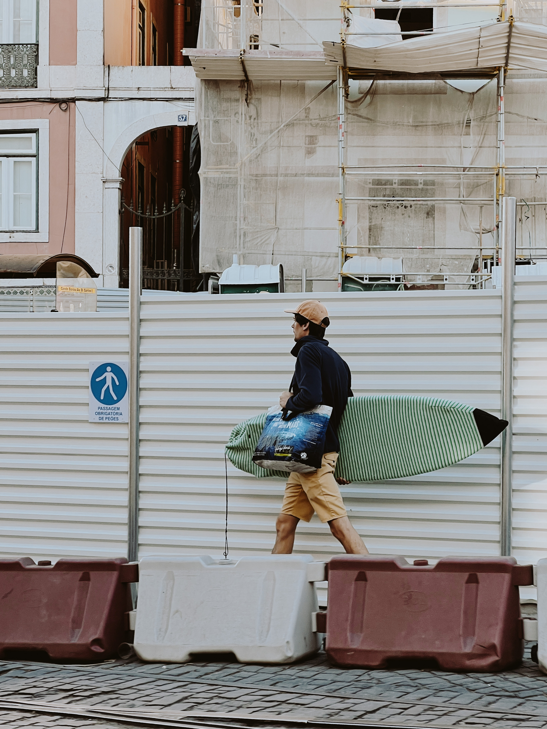 A surfer walks across a messy construction site. 