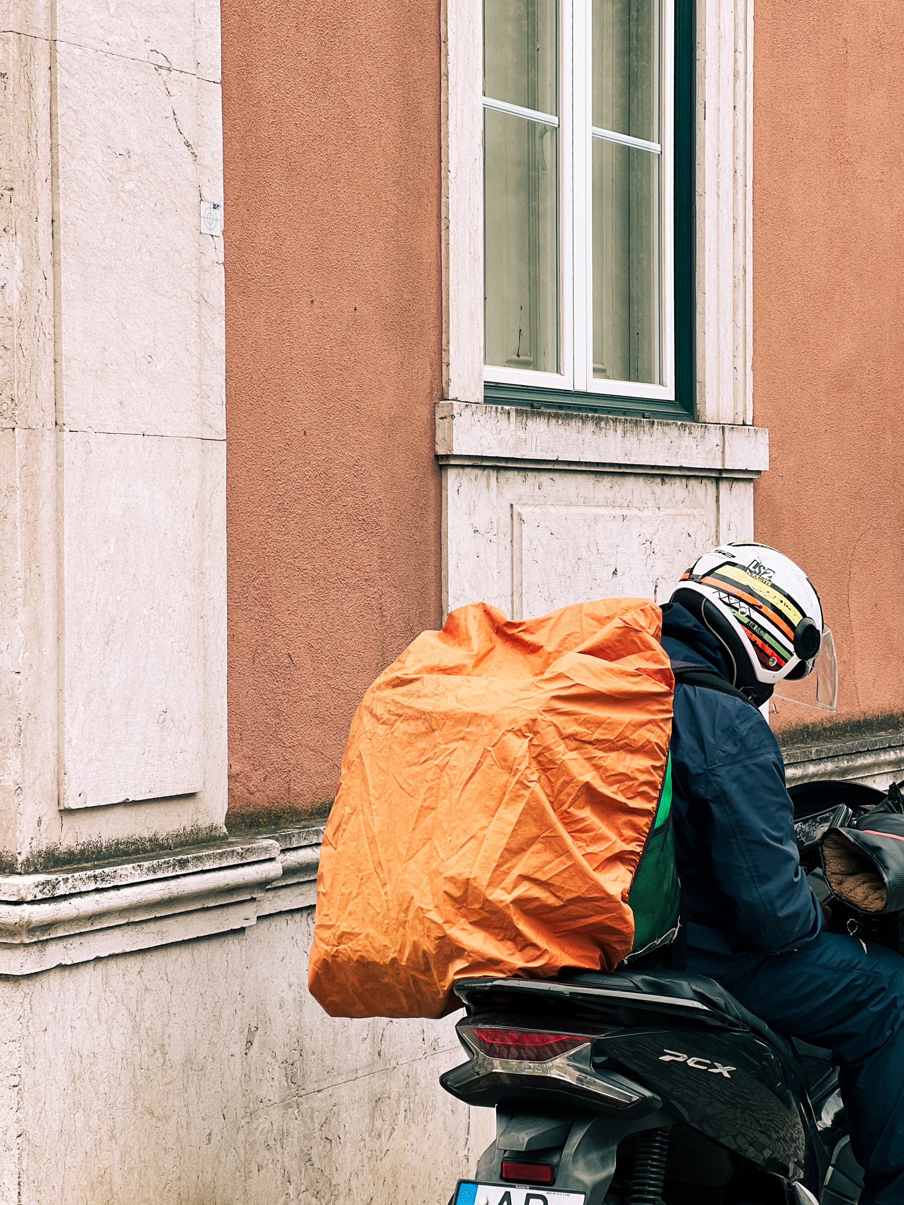 A scooter rider with an orange backpack cover. 