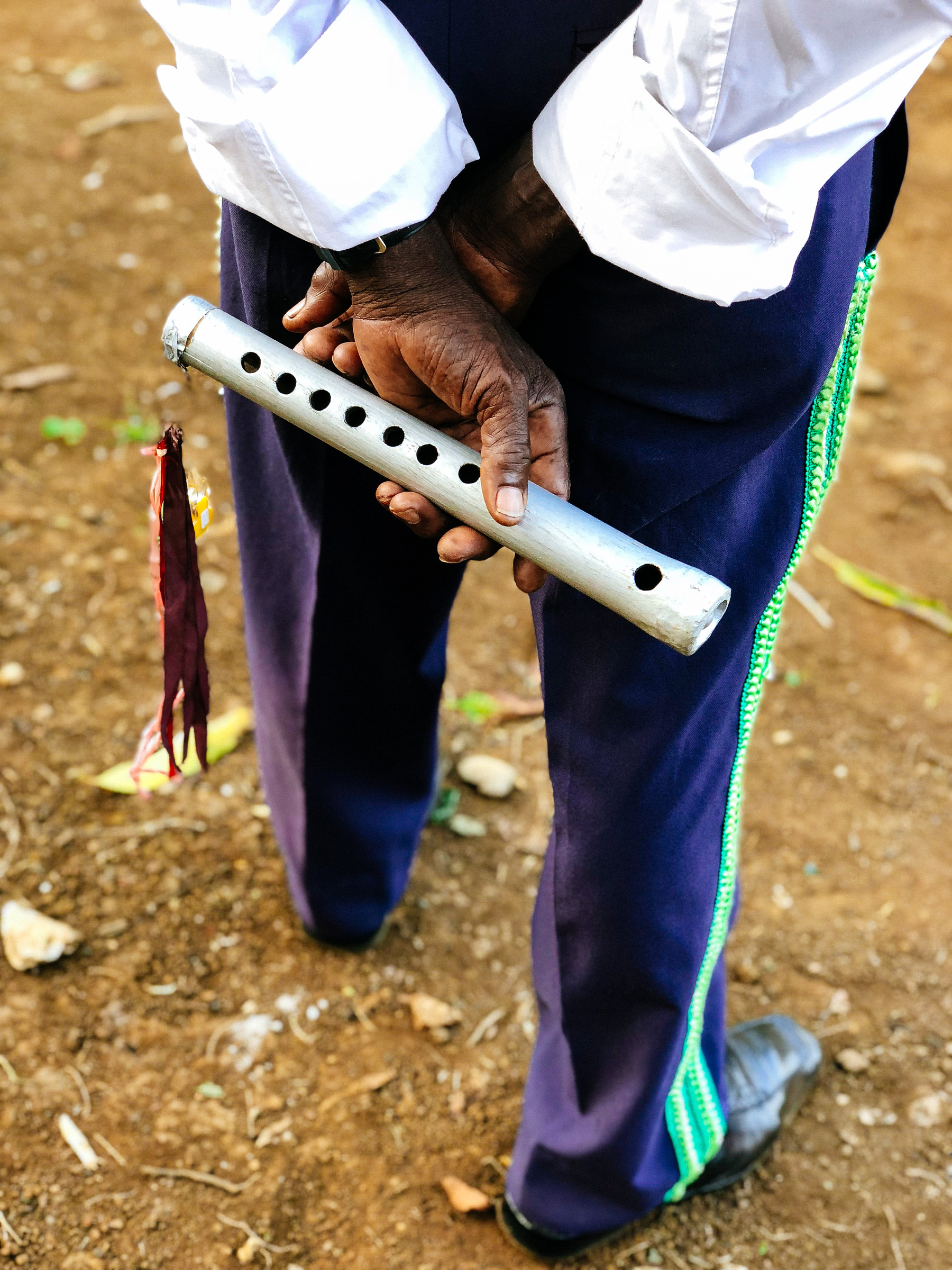 a handmade flute in the hands of a musician. We’re looking down, on his back, he’s holding the instrument behind his back. 
