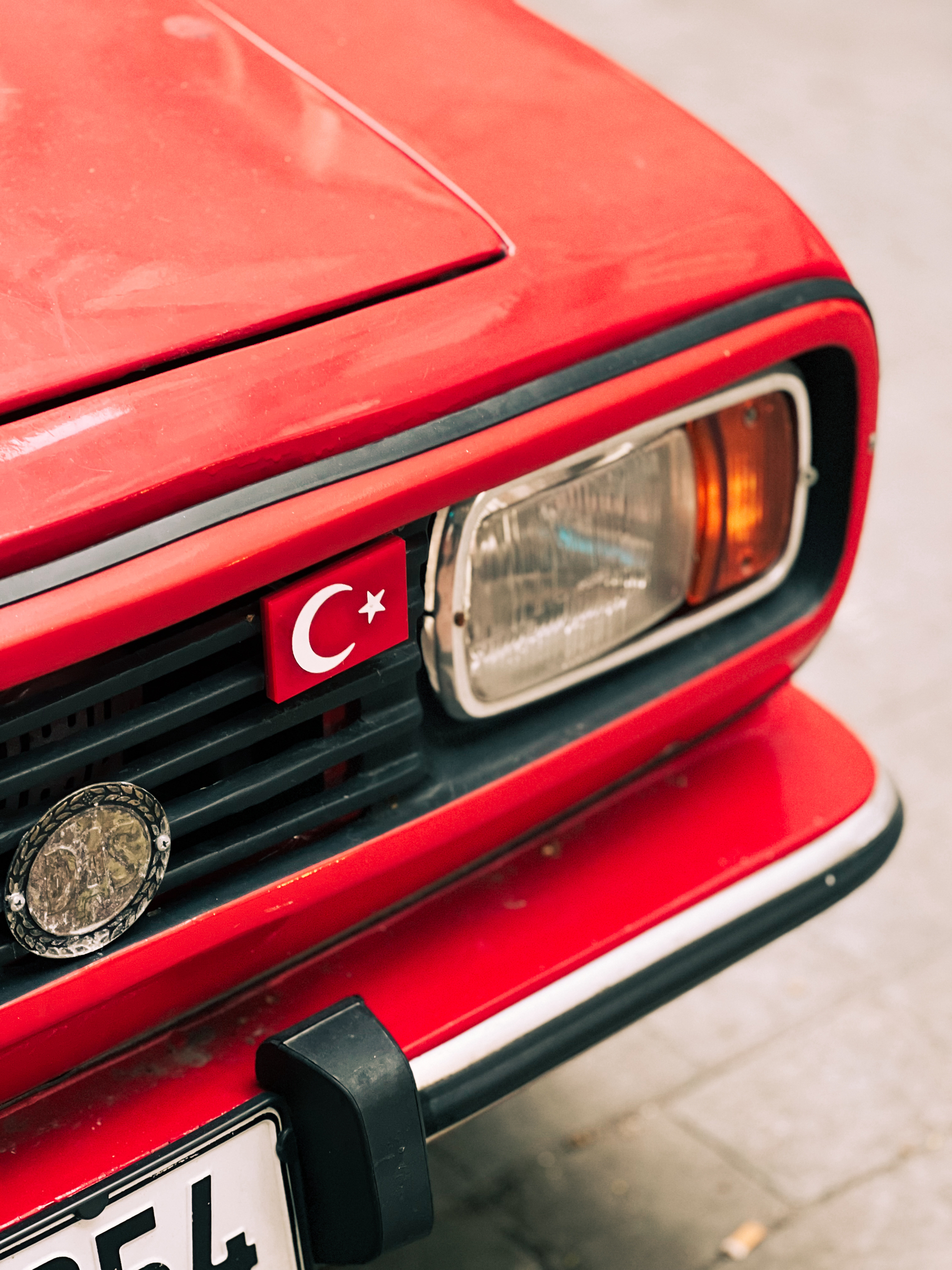 A Turkish flag next to a headlight on a classic car. 
