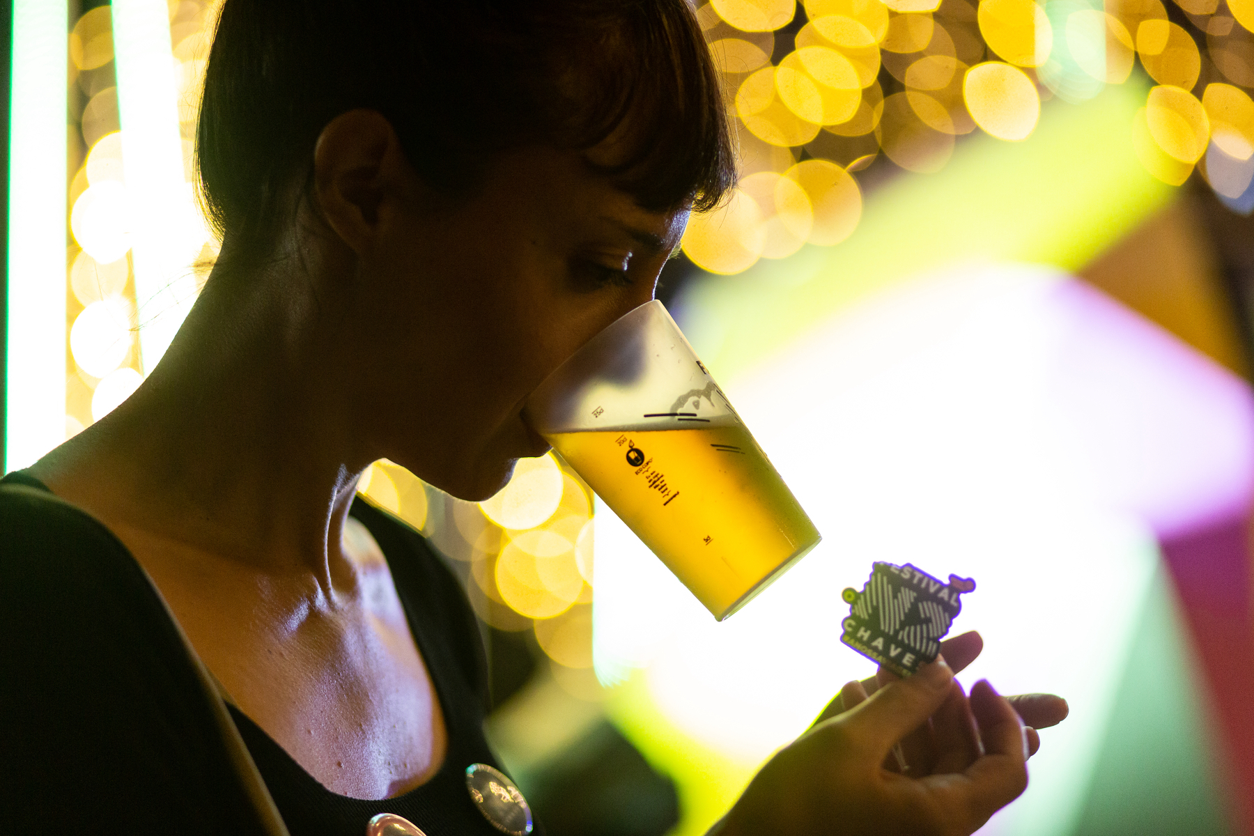 A girl hold a glass of beer with her mouth, and a festival sticker with her hands. 