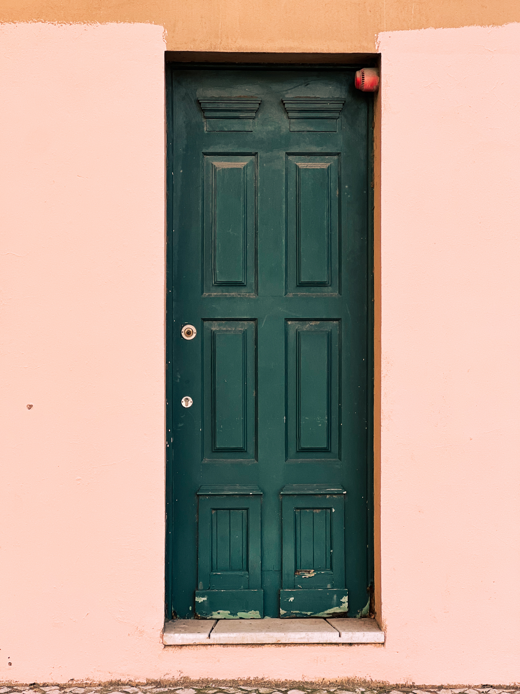 A weathered dark green door set within a peach-colored wall.