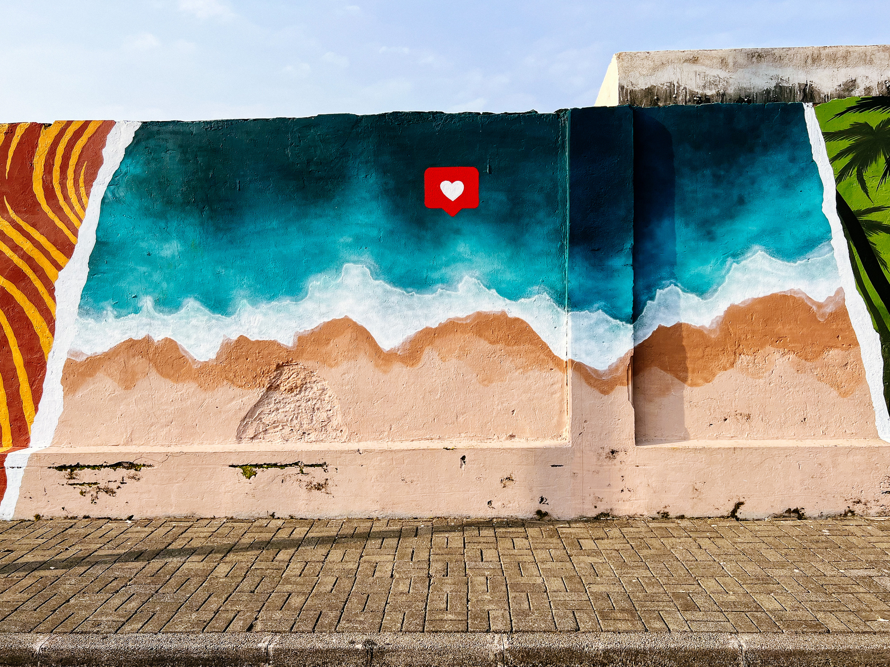 A beach is graffitied into a wall, with an Instagram “Like” icon on top of it. 