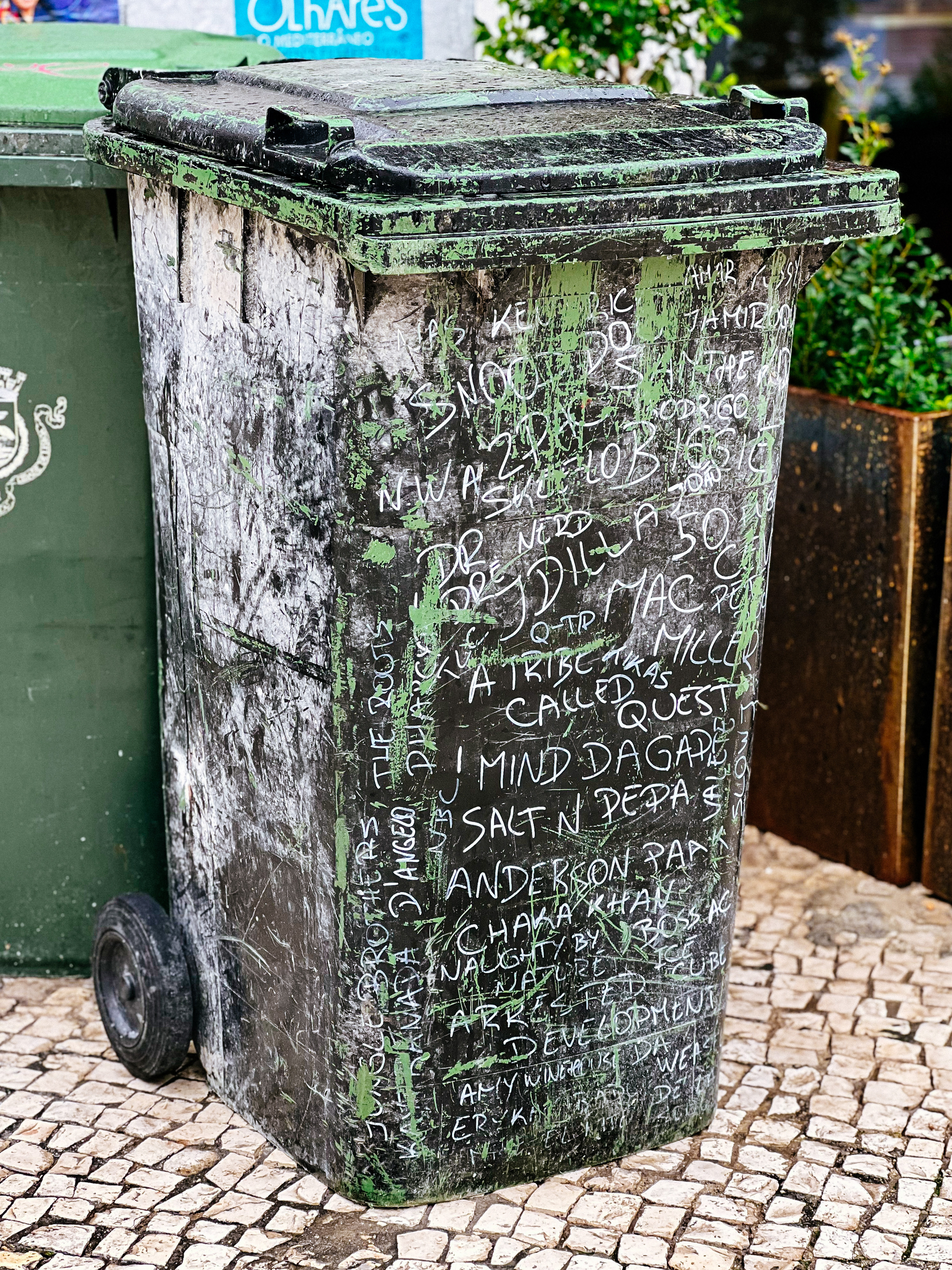 A trash bin covered with band names written in chalk. 
