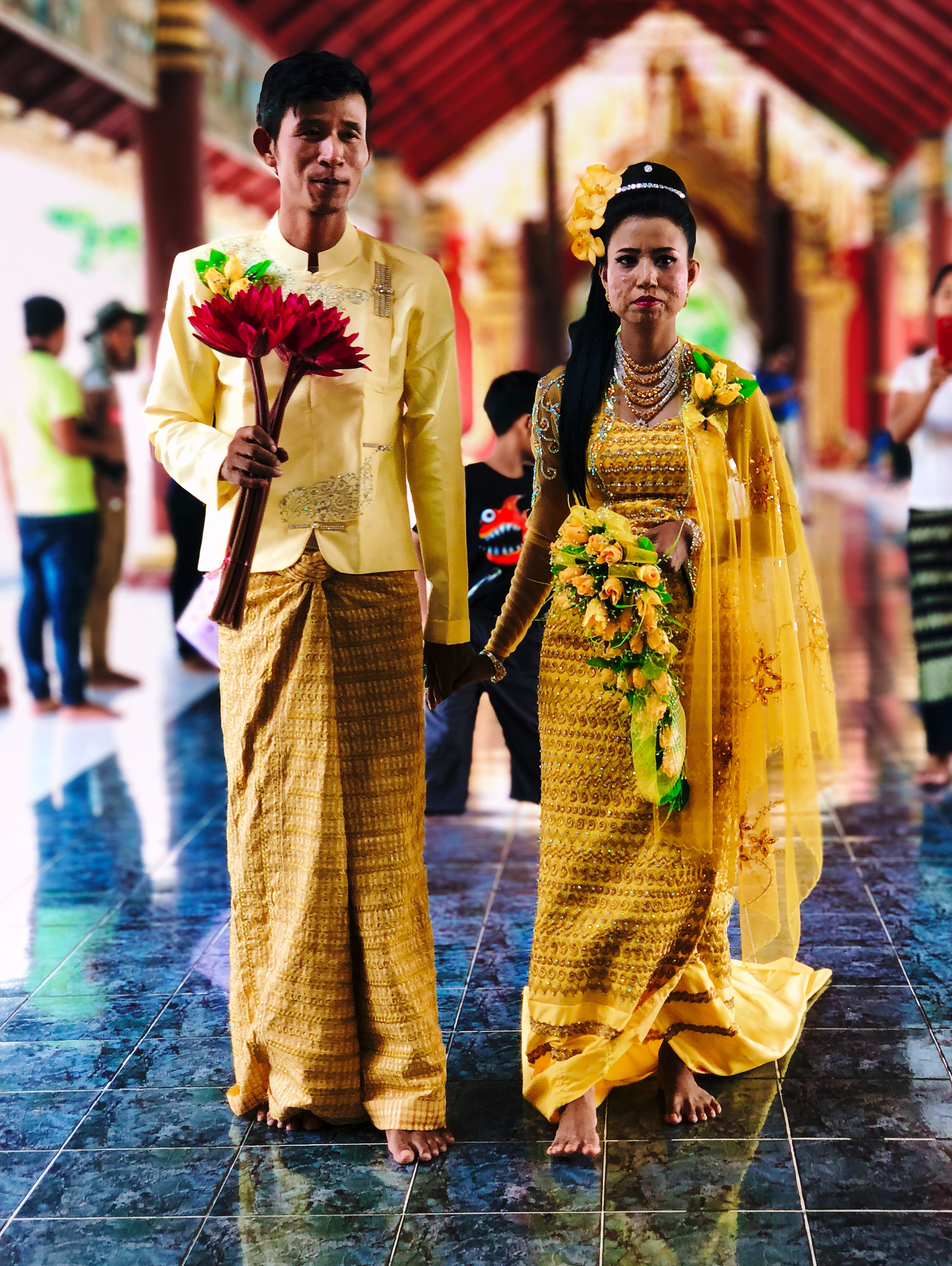 Bride and groom, both dressed in yellow, the man is holding a bouquet. 
