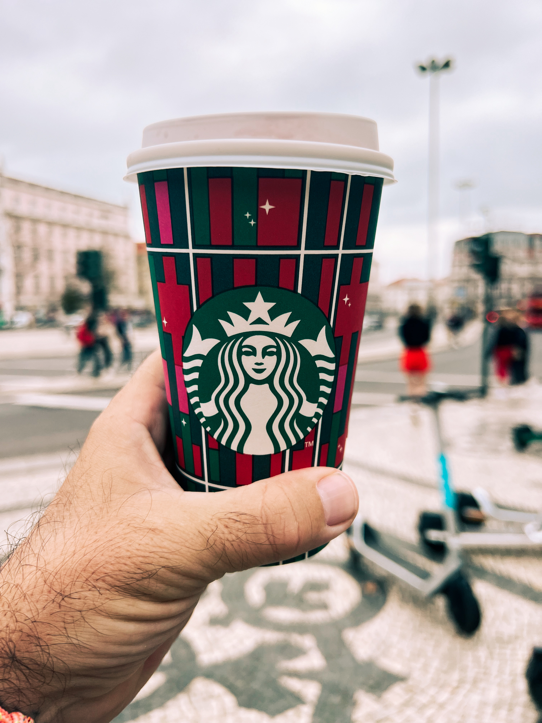 A hand holds a Christmas themed Starbucks cup. 
