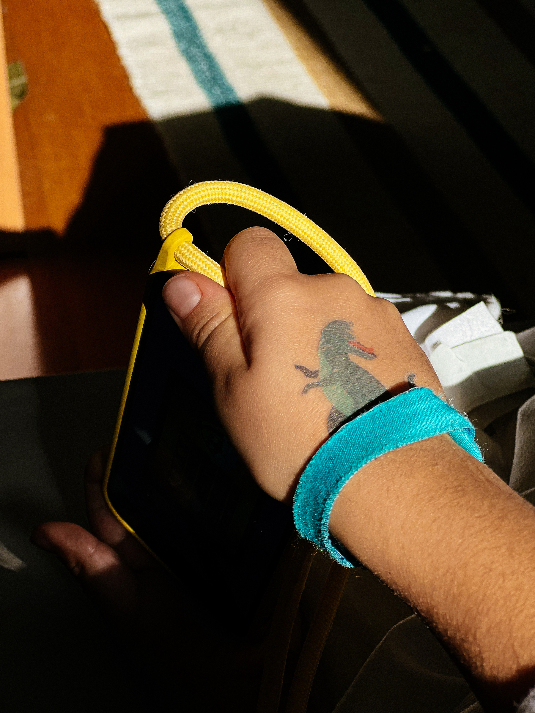 A person&rsquo;s hand holding a yellow jump rope, with a turquoise wristband and a shadow of a dinosaur tattoo on their wrist.