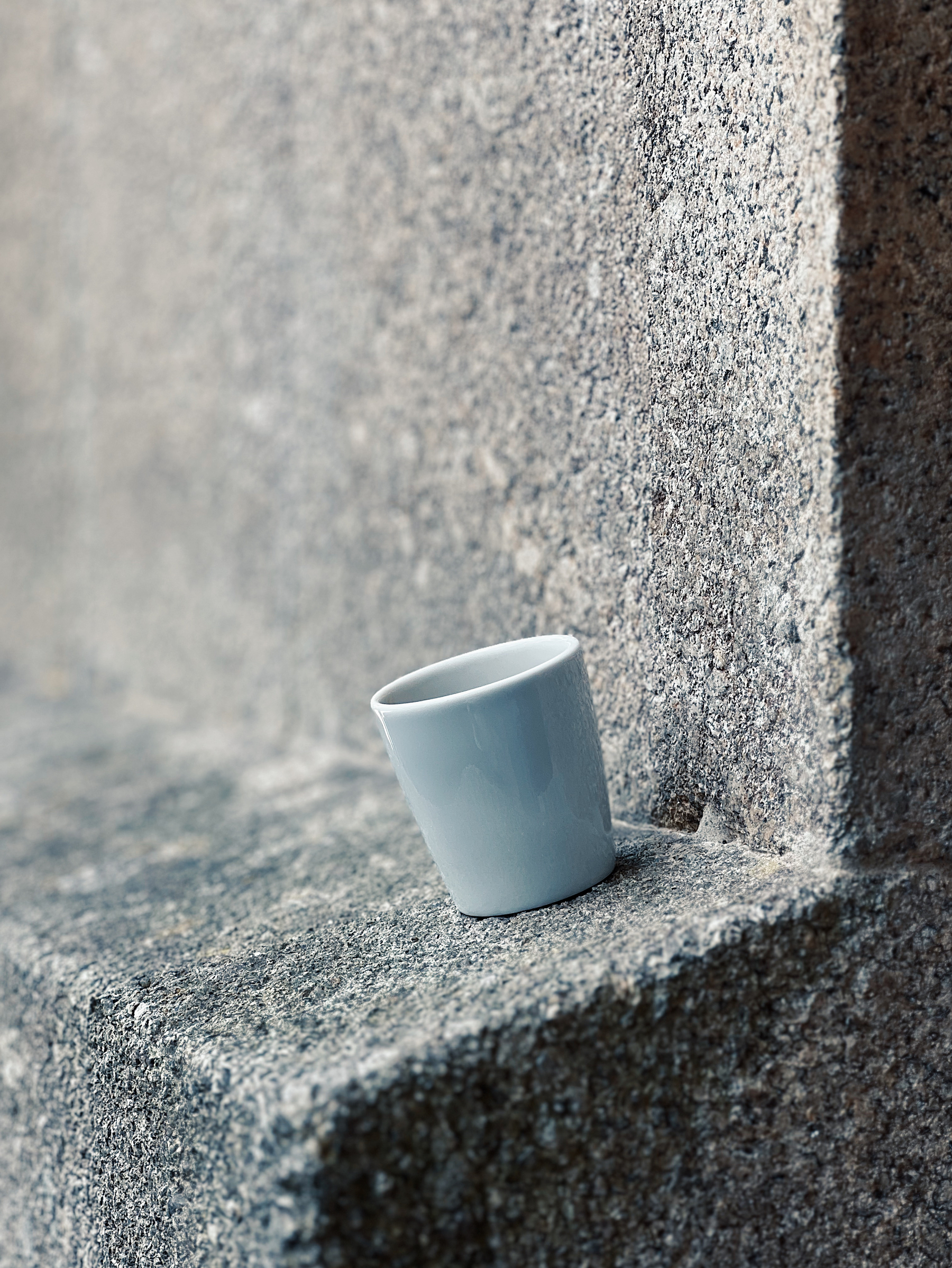 A cup of coffee standing on an uneven ledge. 
