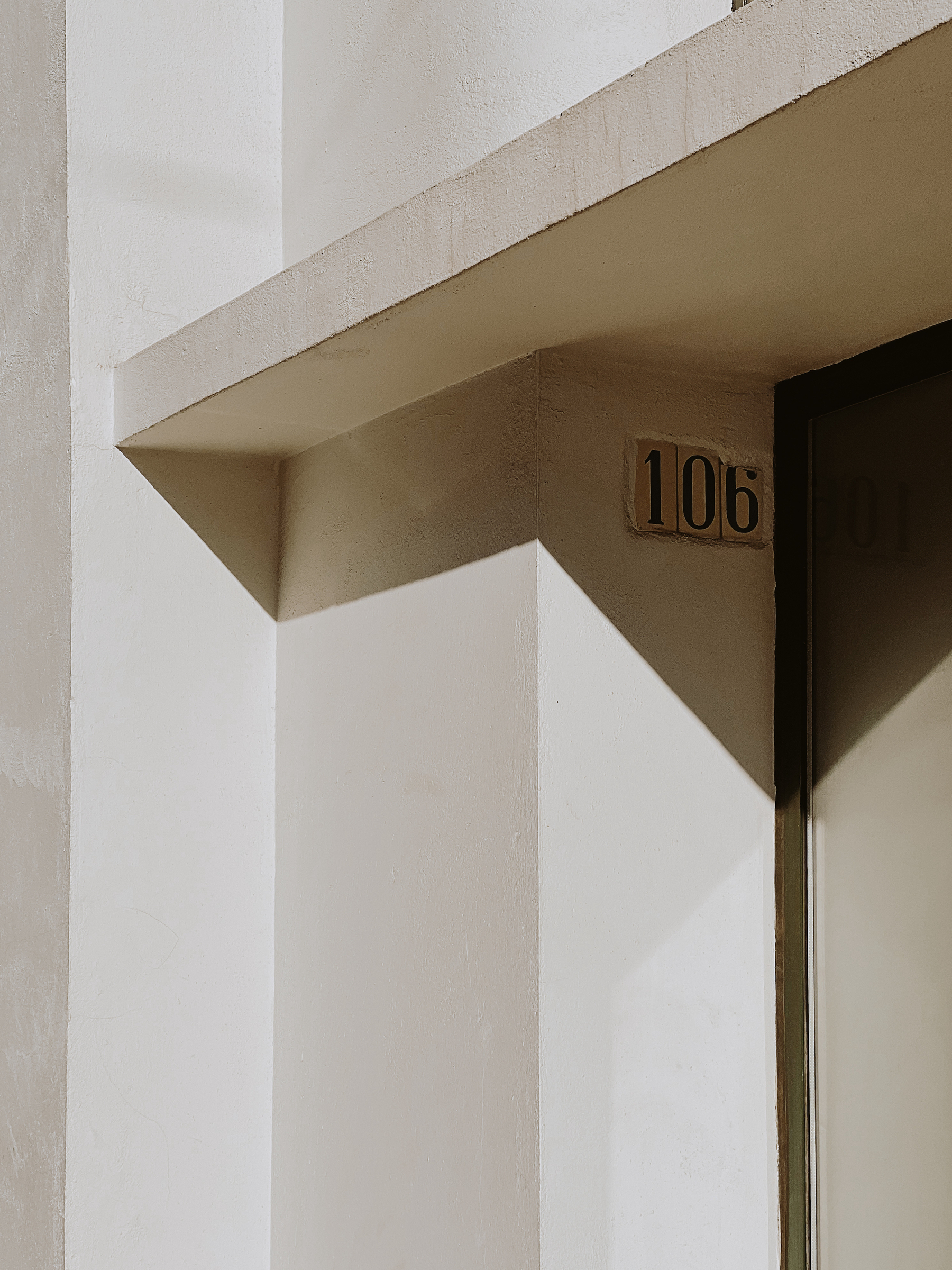 A close-up view of a building entrance with the number 106, featuring strong geometric lines and shadows.