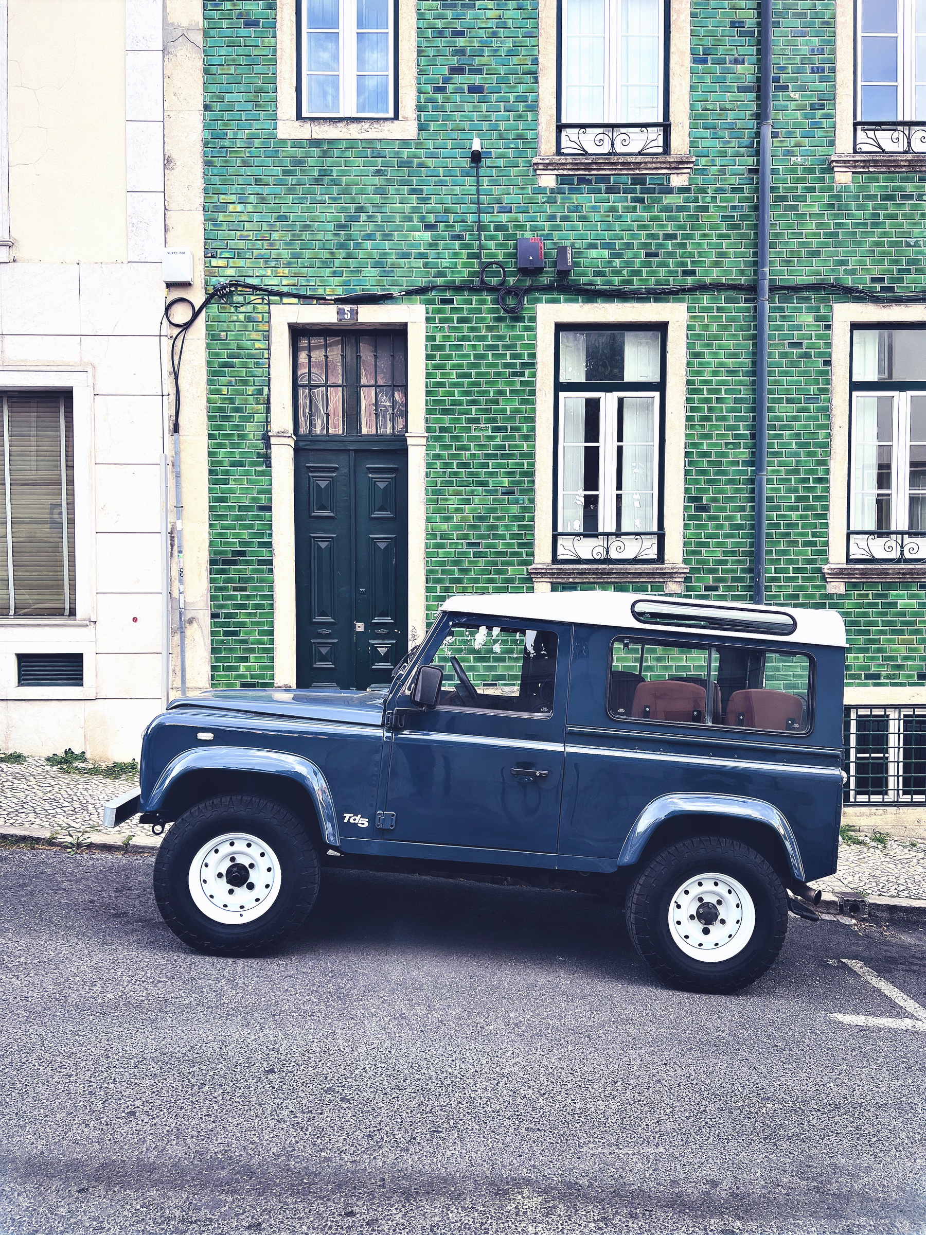 a dark blue Land Rover against a green building