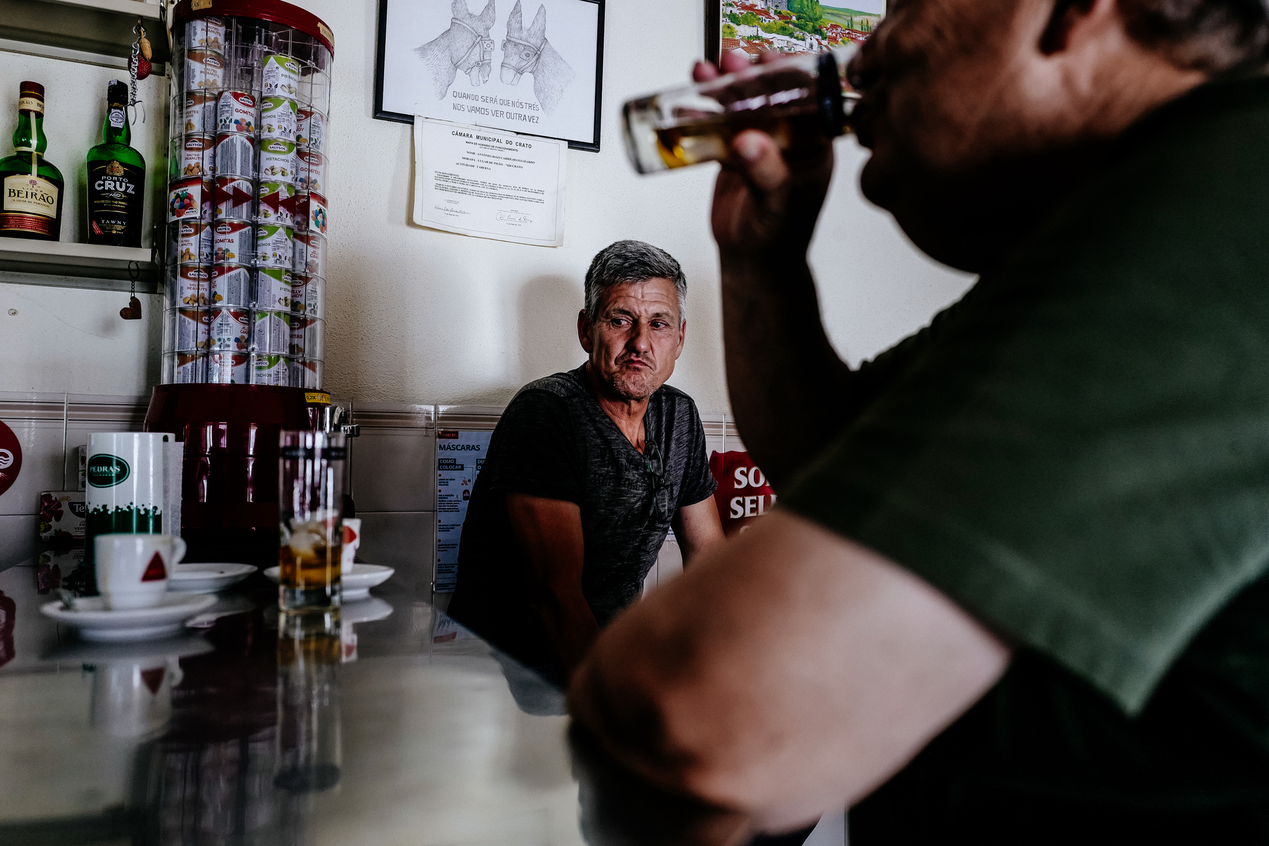 A man has a drink while sitting at the counter, another looks at something outside the frame. 