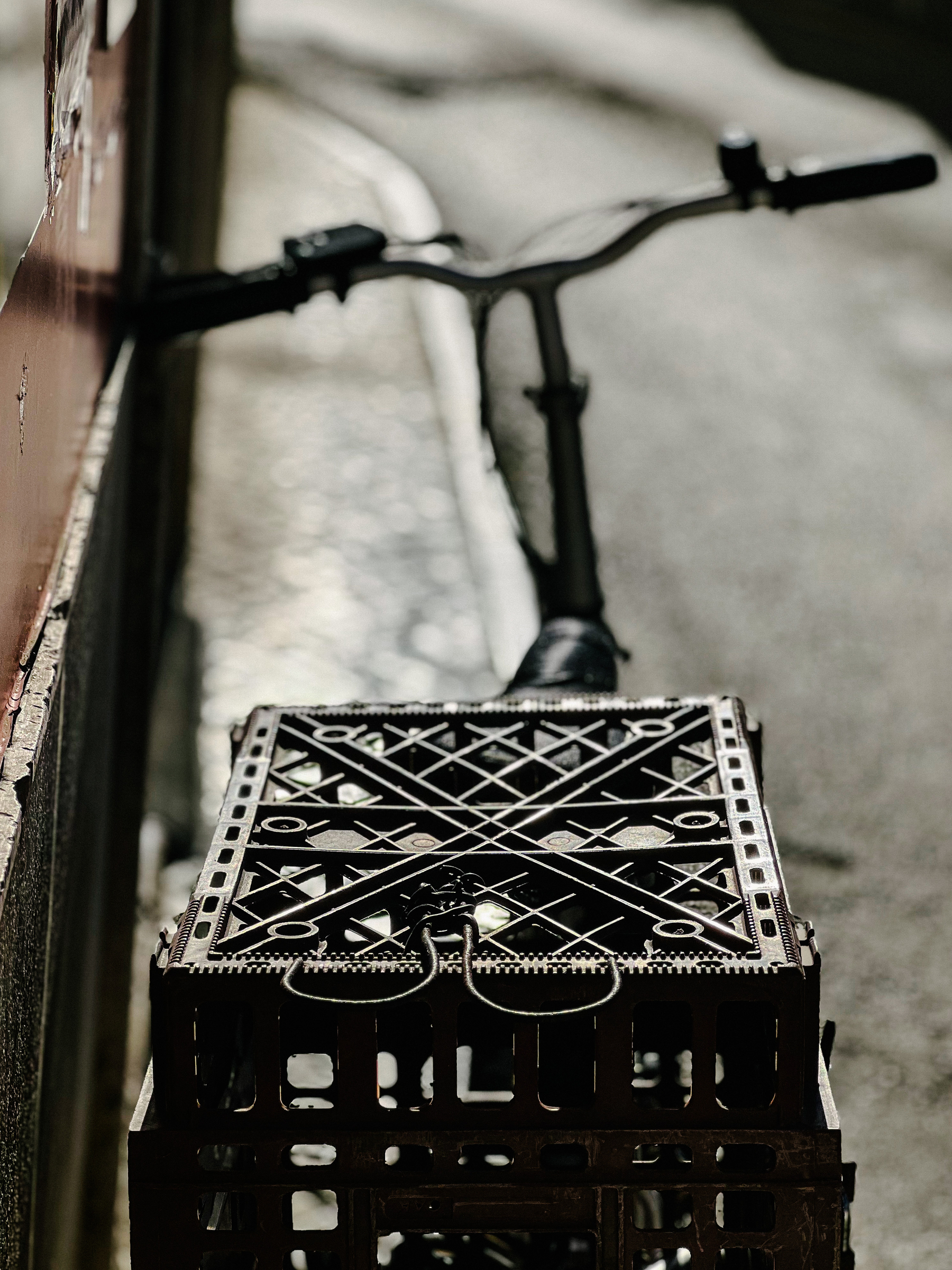 A bicycle parked against a wall, with a sort of basket in the back. 