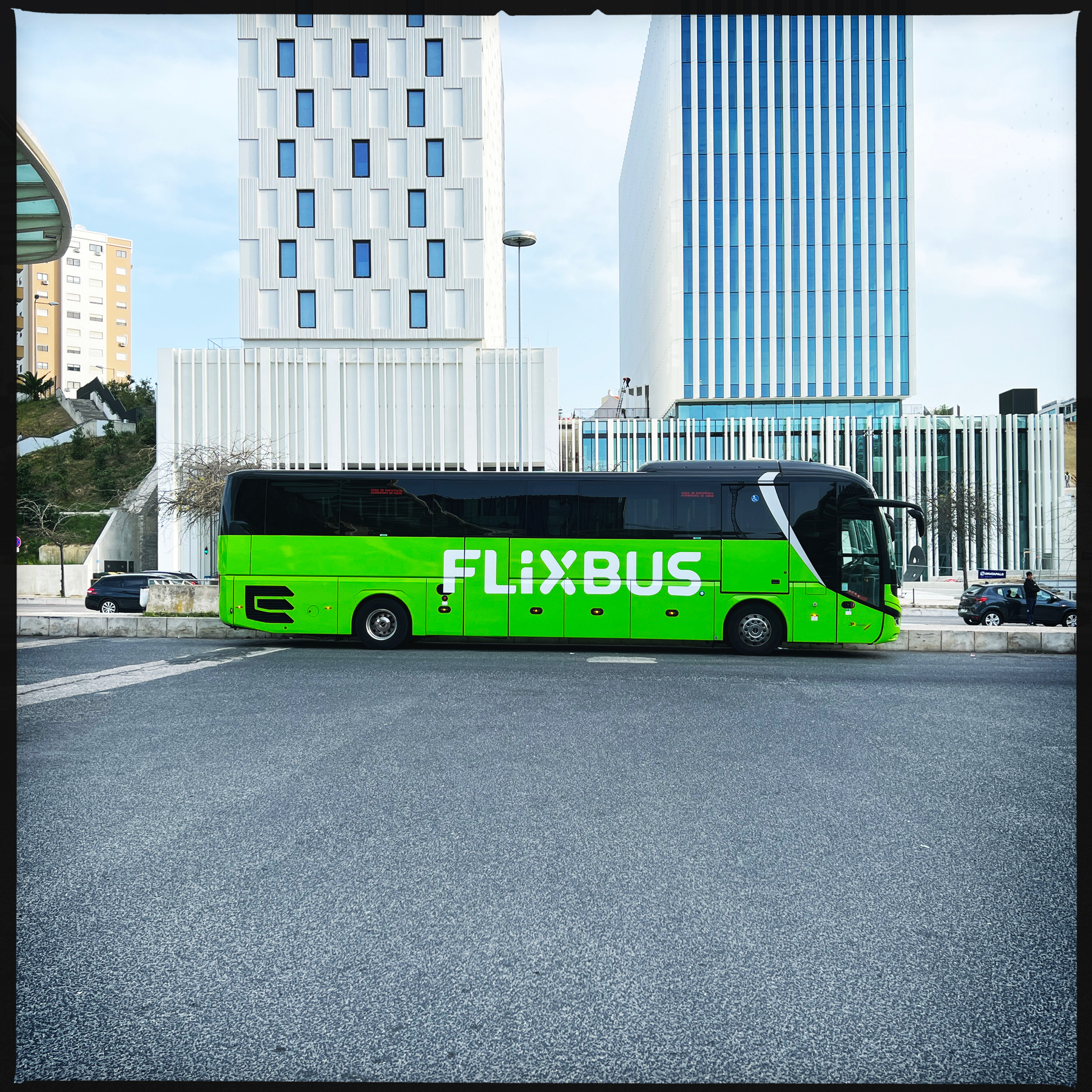 a green bus with “flixbus” written on the side, parked next to modern looking buildings