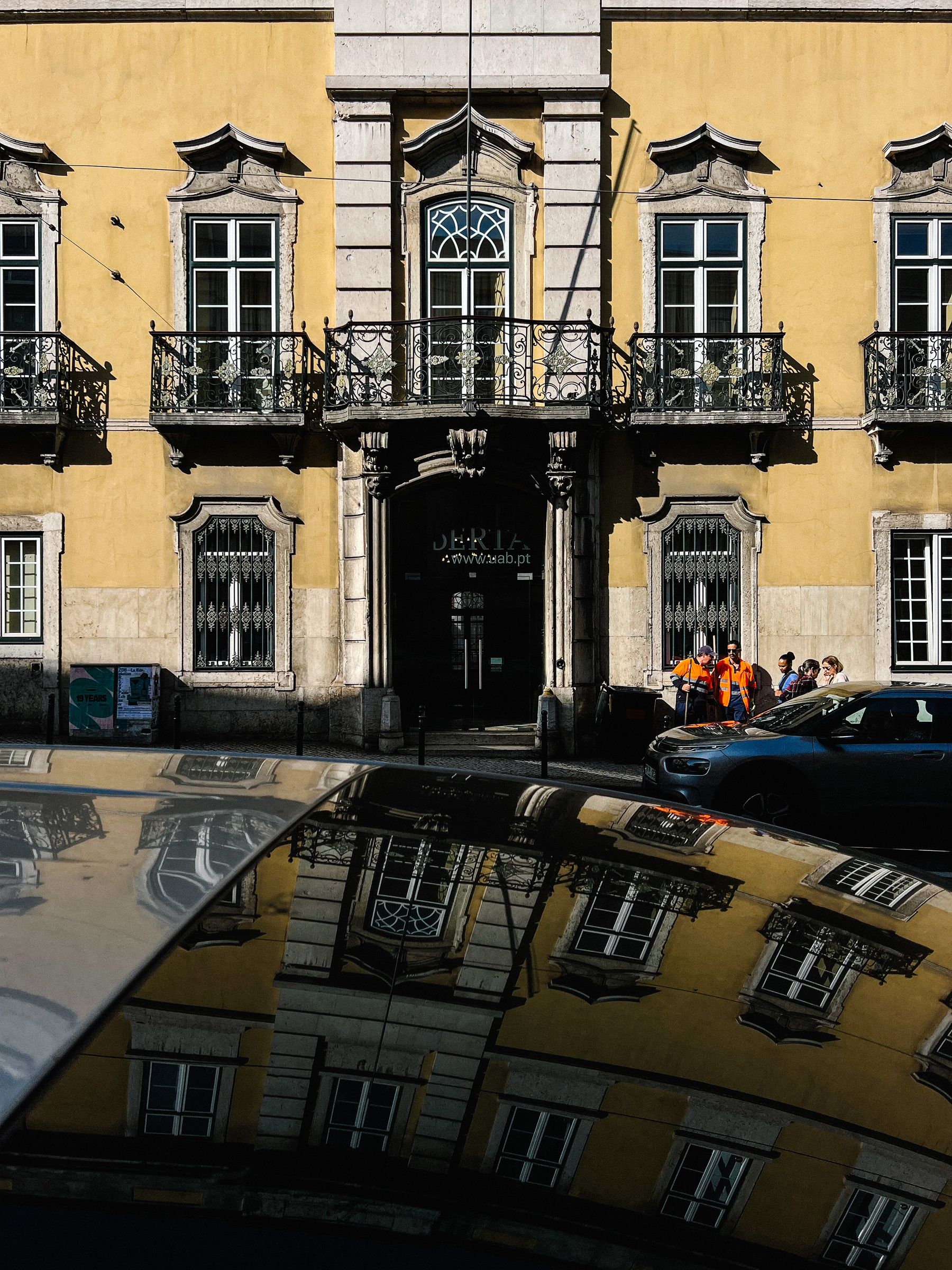 A yellow building, also reflected on a car in the foreground. 