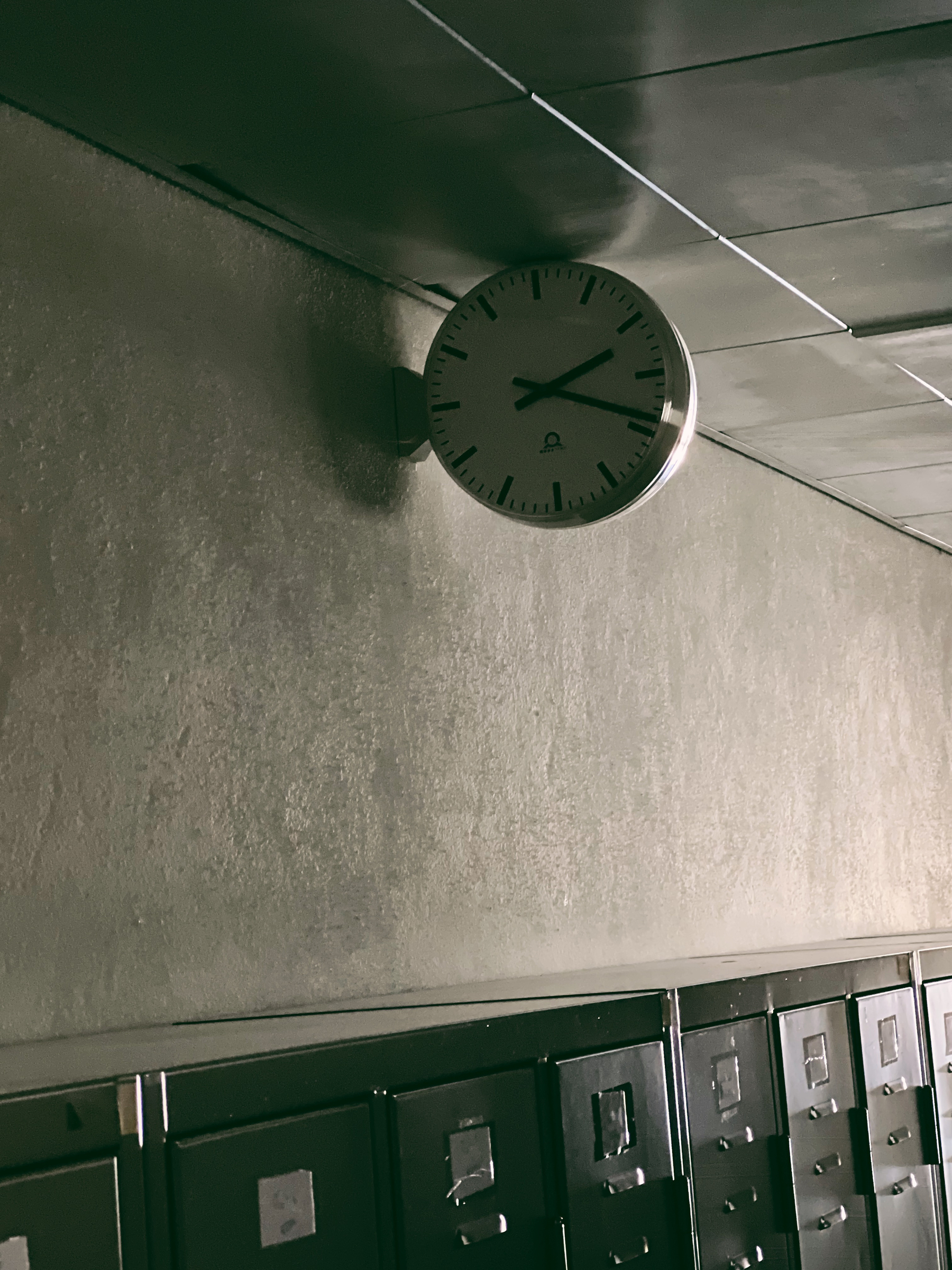 A clock on a wall, above school lockers. 