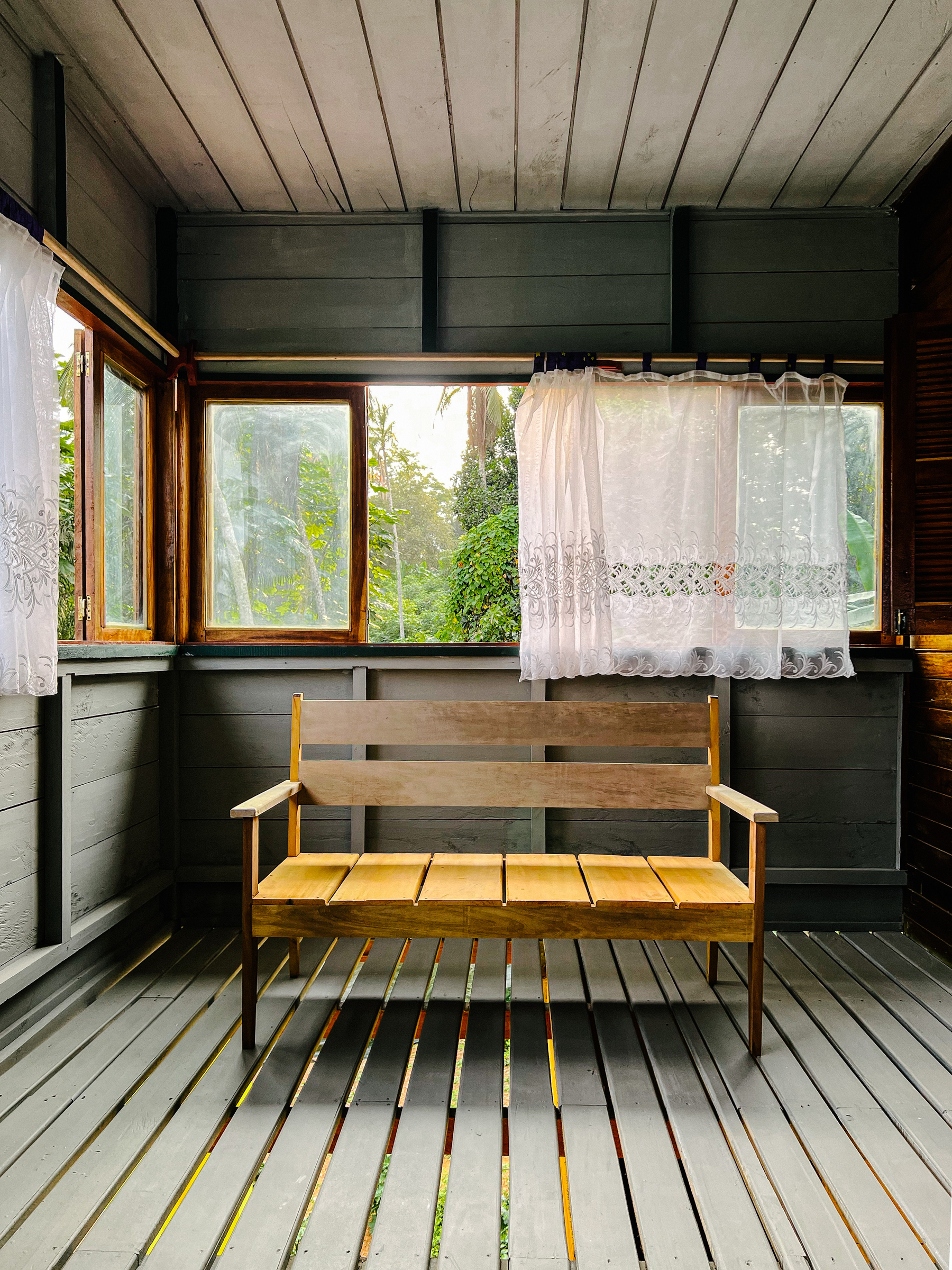 A simple room, all made of wood, with a bench and windows looking out to the rainforest. 