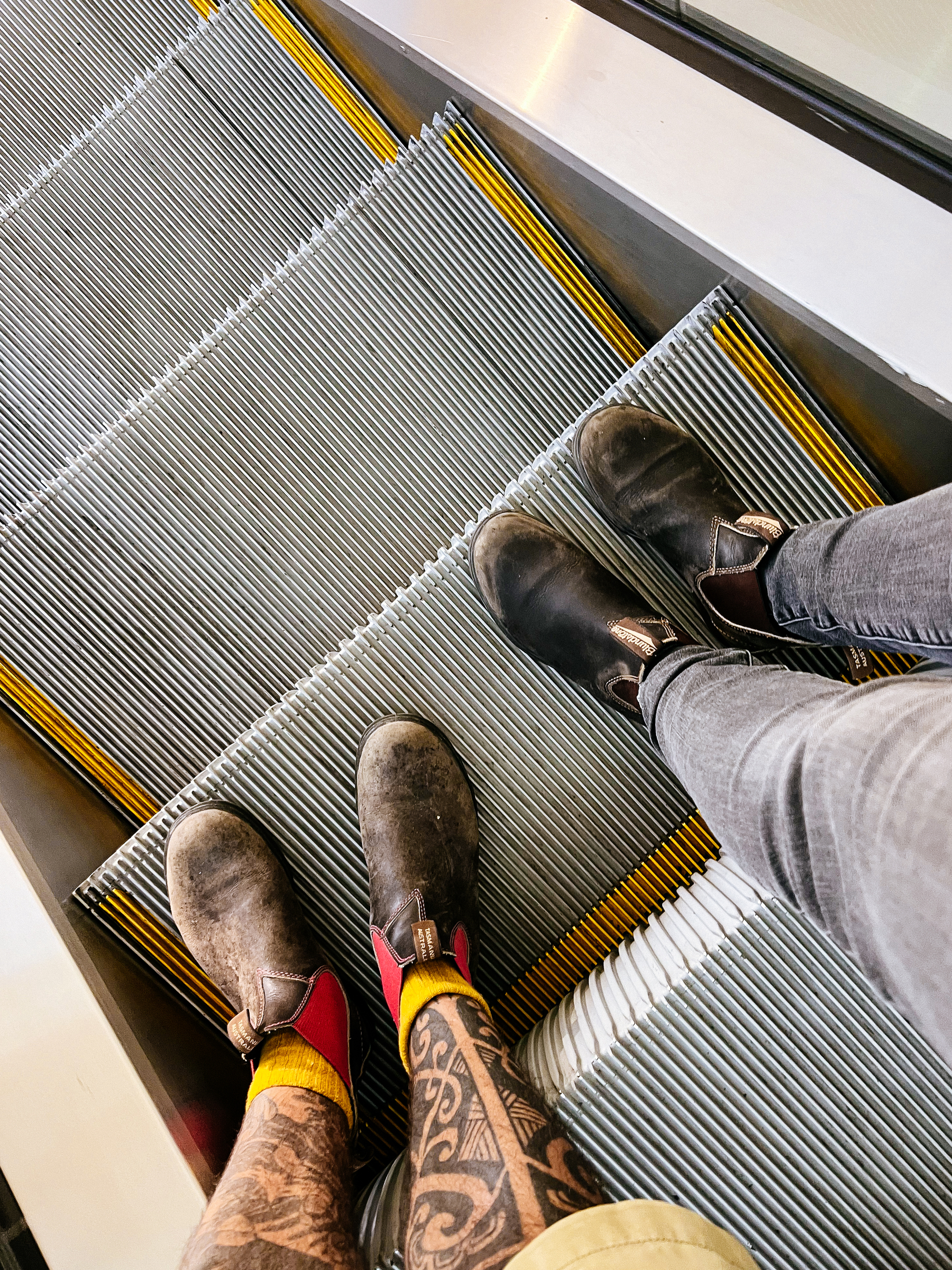 Looking down on two pairs of legs, on an escalator.