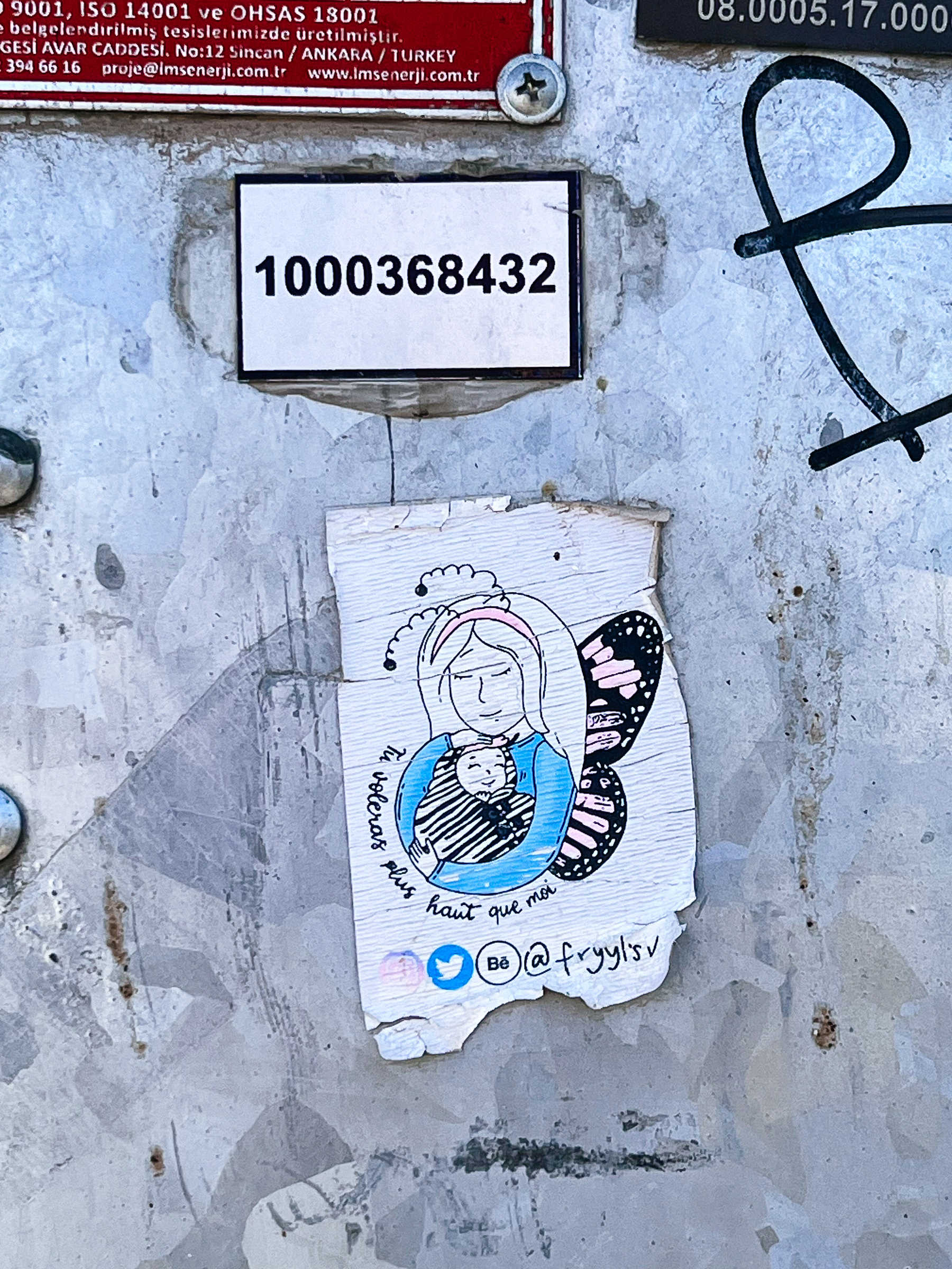 A sticker with the drawing of an fairy holding a child, and the text “you will fly higher than me” in French. 