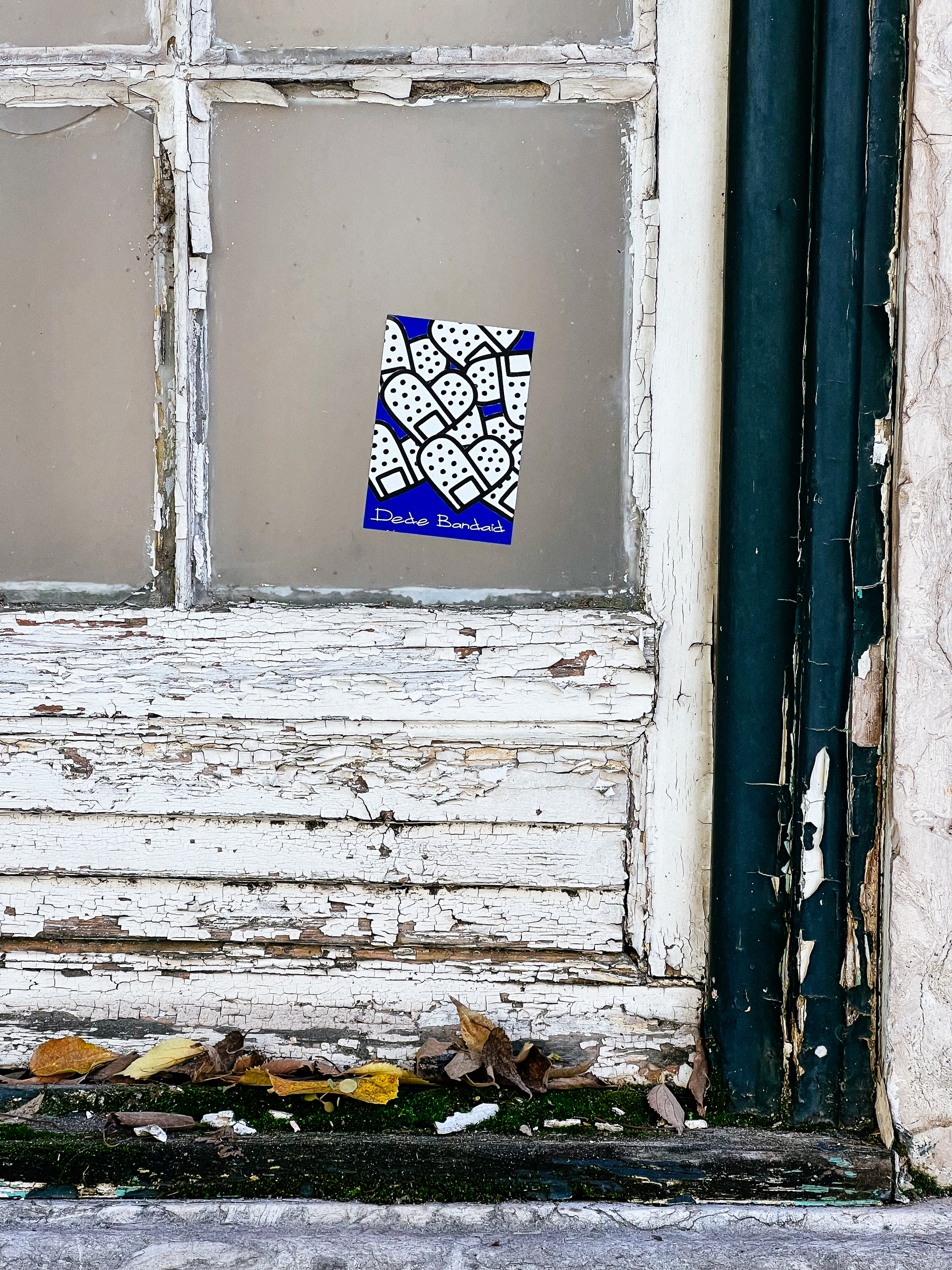 White bandaids on a blue background. A sticker, on an abandoned building’s window. 