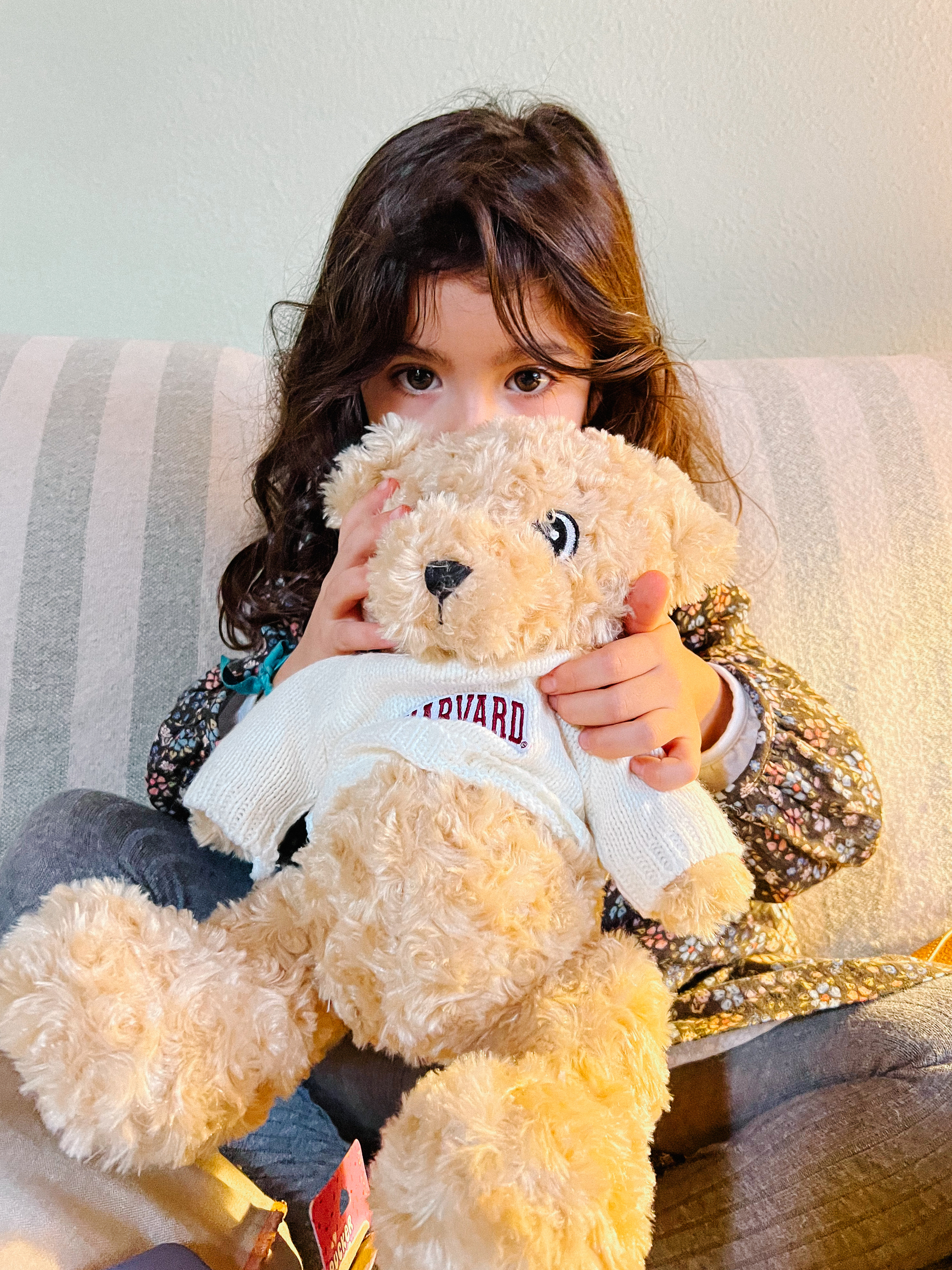 A young child holding a teddy bear while sitting on a couch.