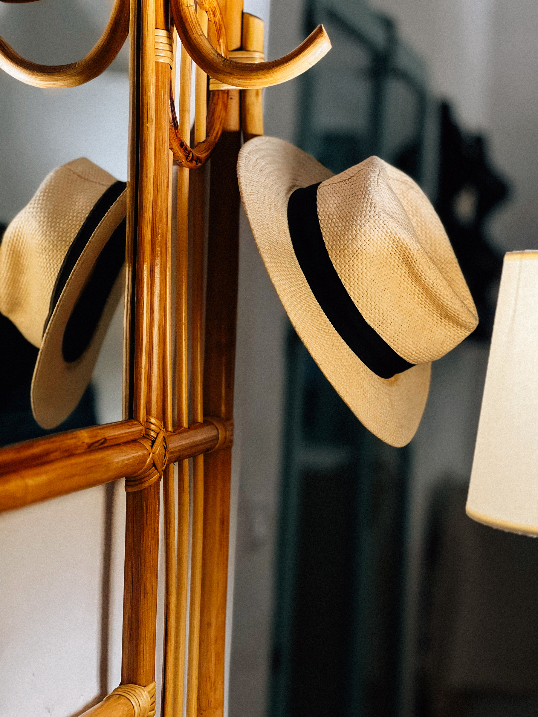 A wooden coat rack with a straw hat hanging on its hooks, with a warm light illuminating the scene.
