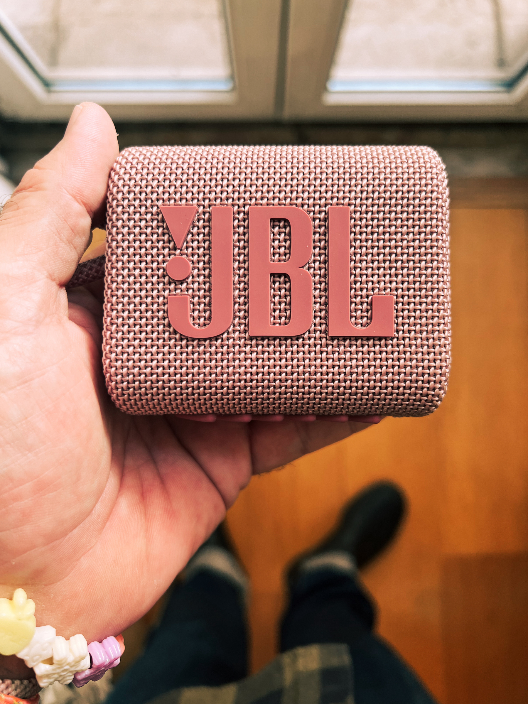 A close-up of a hand holding a pink JBL portable Bluetooth speaker.