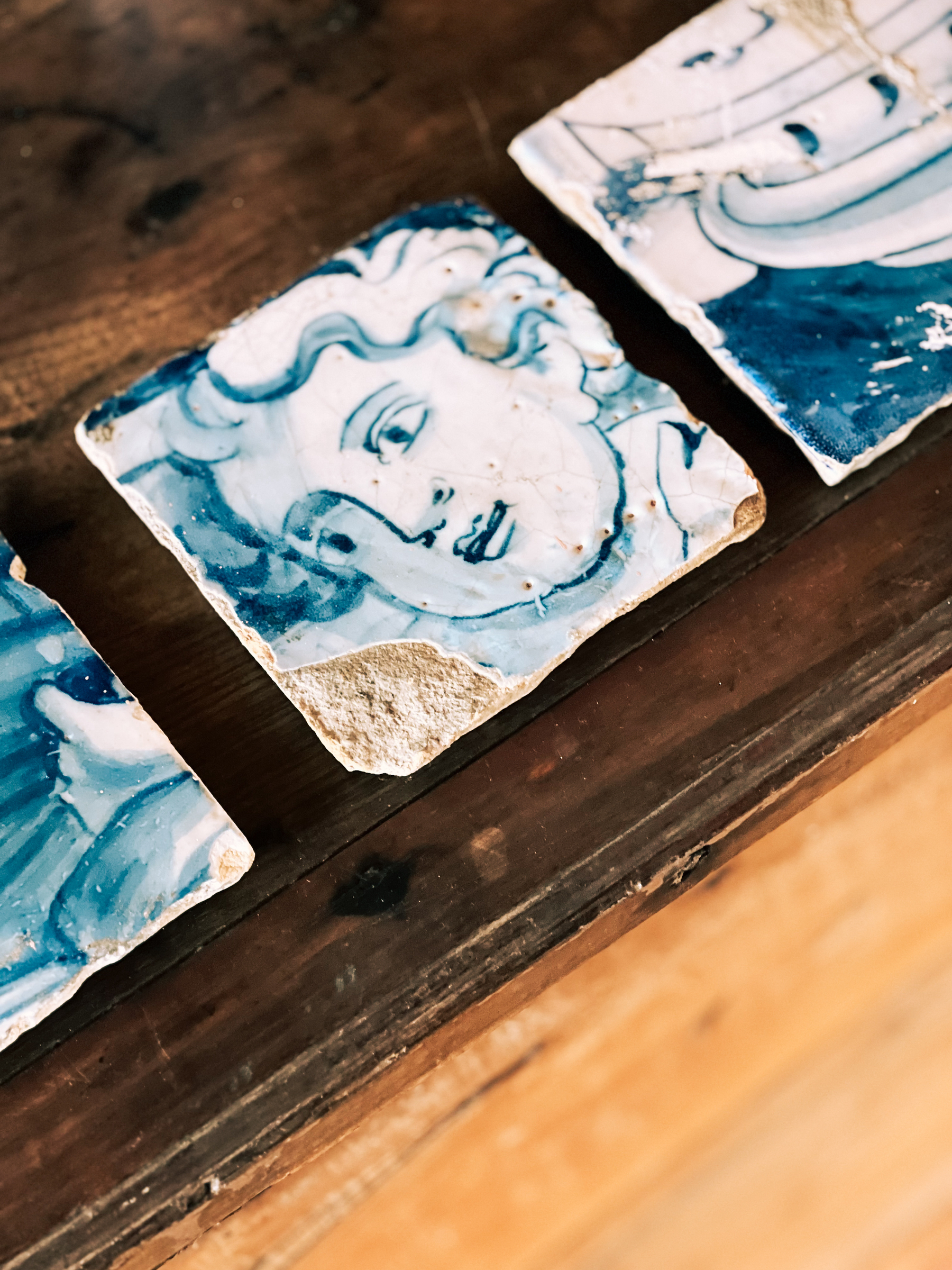 Blue and white ceramic tiles with artistic representations of classical faces displayed on a wooden surface.